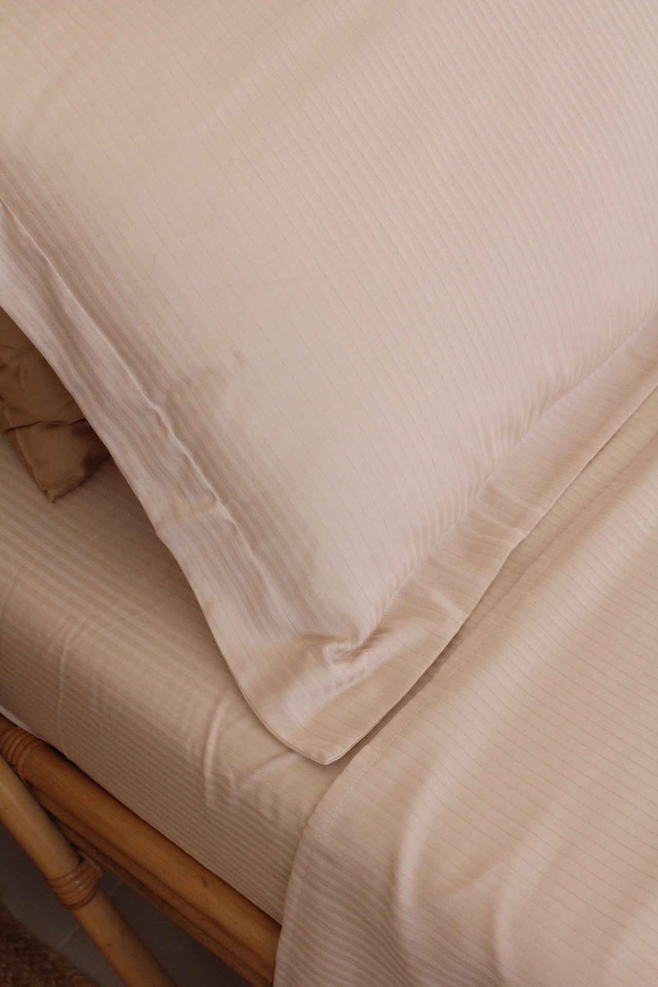 Conjunto cama bege riscas finas com almofada e lençol sobre cama de madeira clara