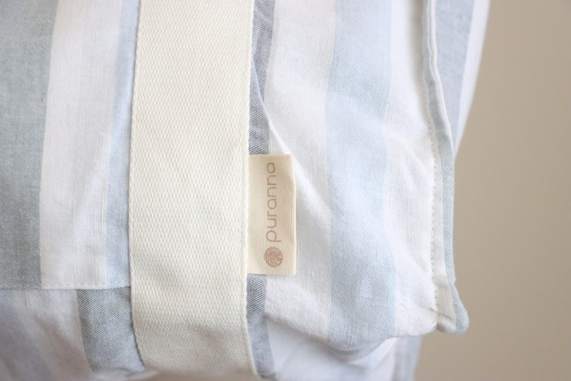 Almofada branca com riscas azuis claras e etiqueta purcotton