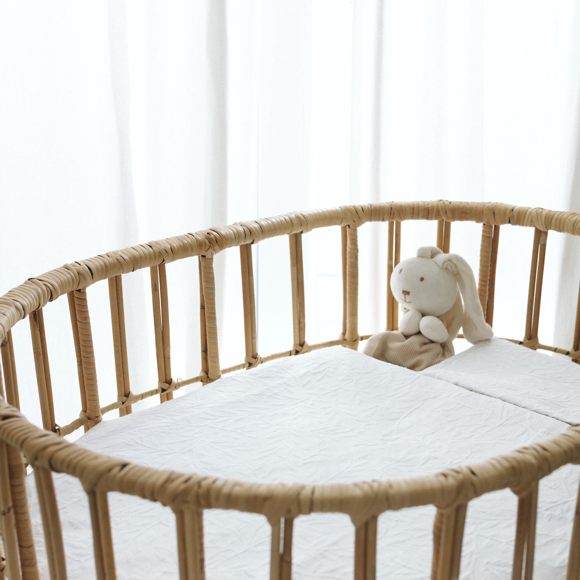 Berço oval de vime com colchão branco e boneco de peluche em forma de coelho