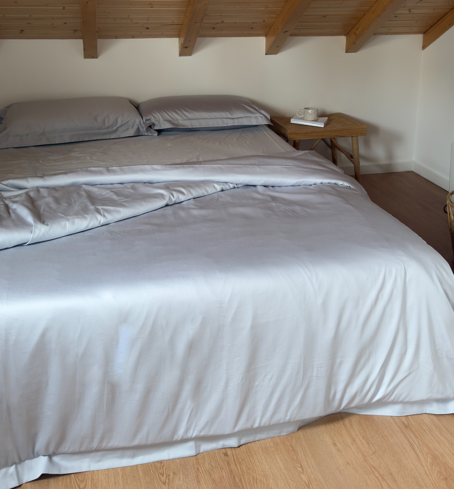 Cama de casal com roupa de cama cinza claro em quarto minimalista com teto de vigas de madeira