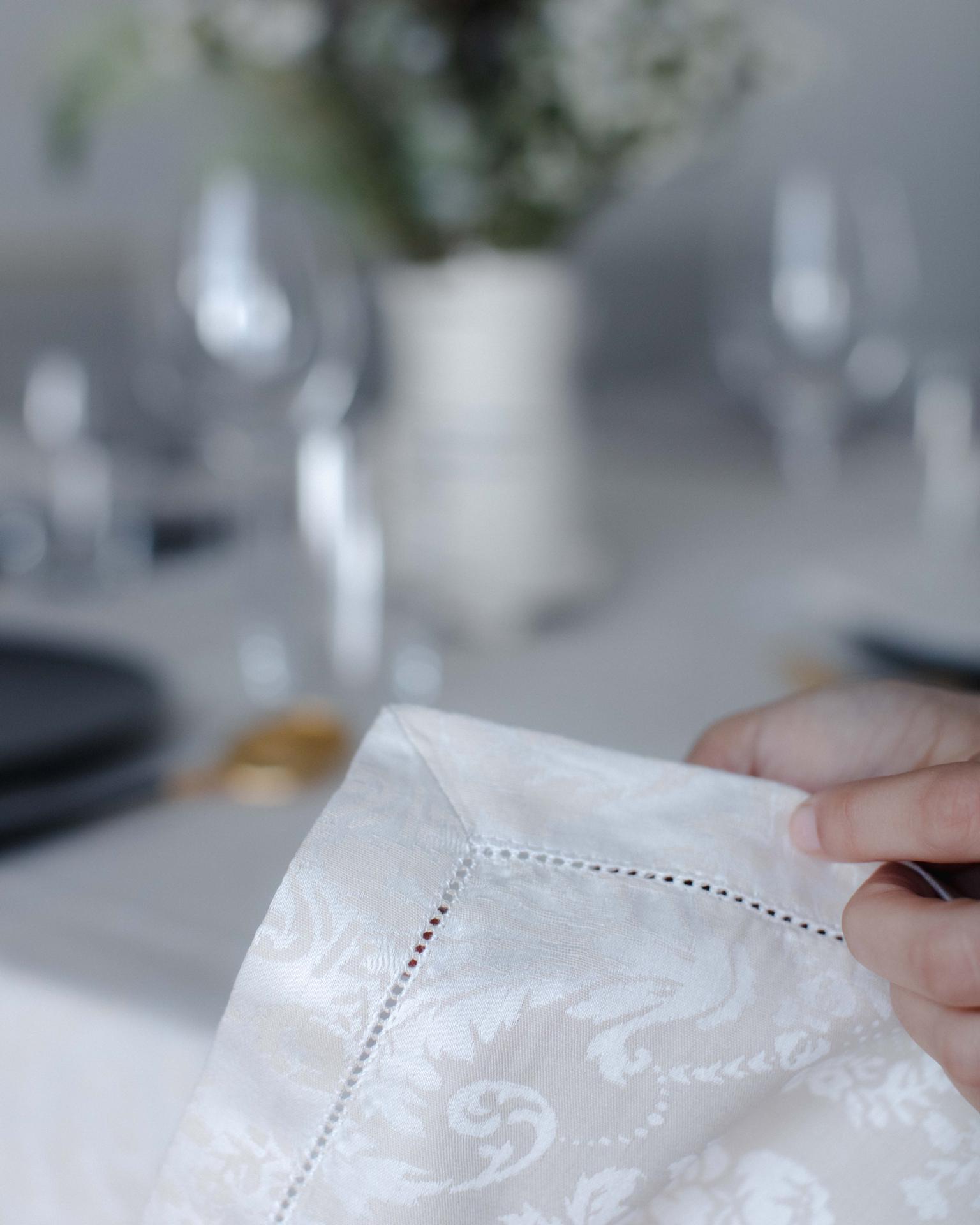 Pano de mesa branco com padrão floral e borda perfurada segurado por uma mão