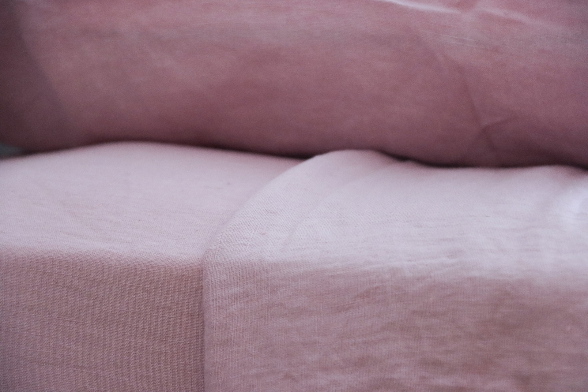 Sofá rosa claro em tecido com textura lisa e almofadas de assento e encosto