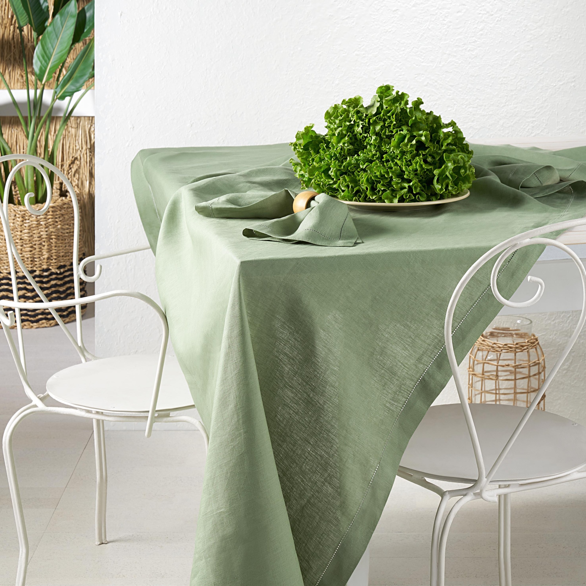 Mesa com toalha verde, prato com alface e cadeiras brancas em ambiente minimalista