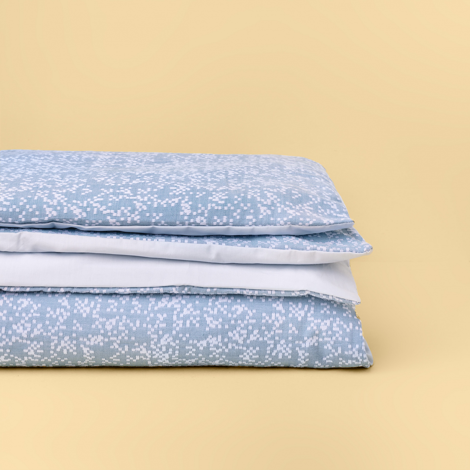 Edredão azul claro com padrão de pontos brancos dobrado sobre fundo amarelo