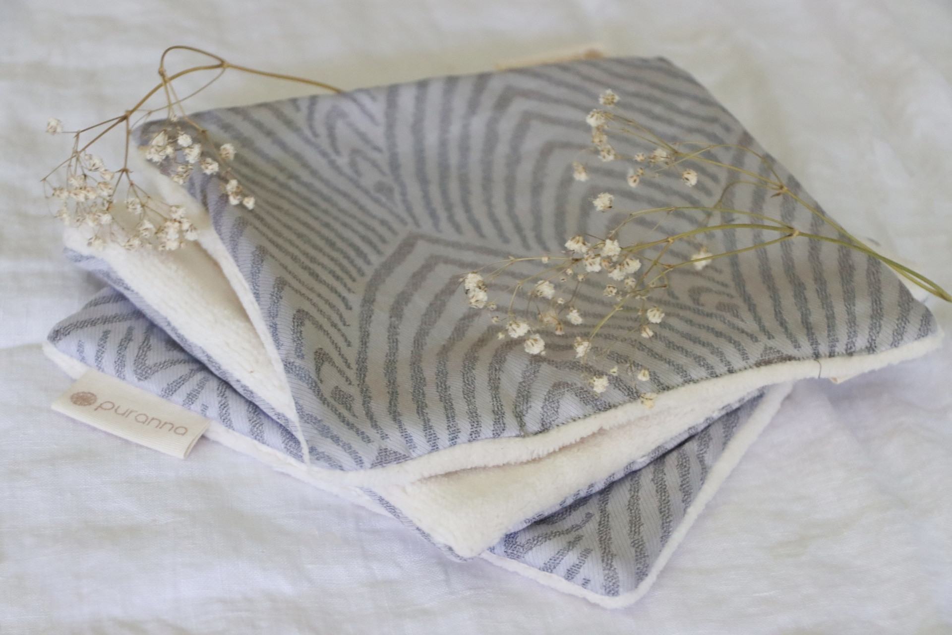 Manta cinzenta com padrão tipo zebra sobre fundo branco com raminhos secos