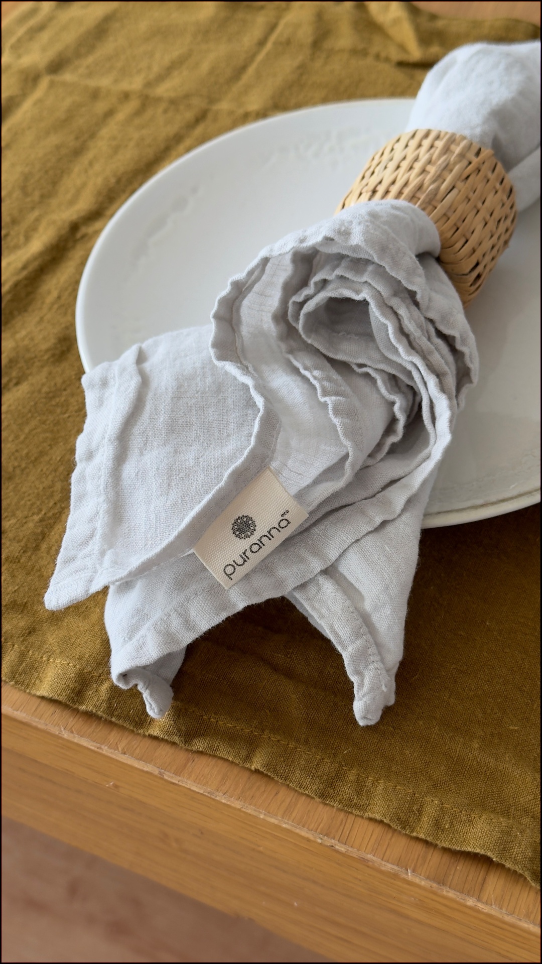 Guardanapo cinzento com suporte trançado sobre prato branco e toalha castanha