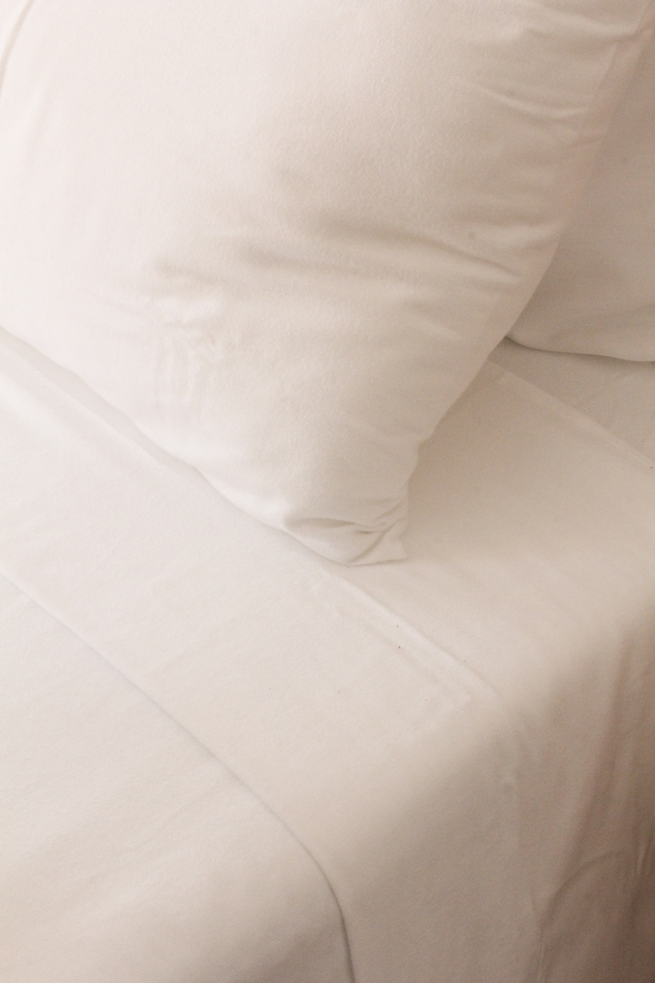 Travesseiro e lençol bege claro com textura lisa em cama