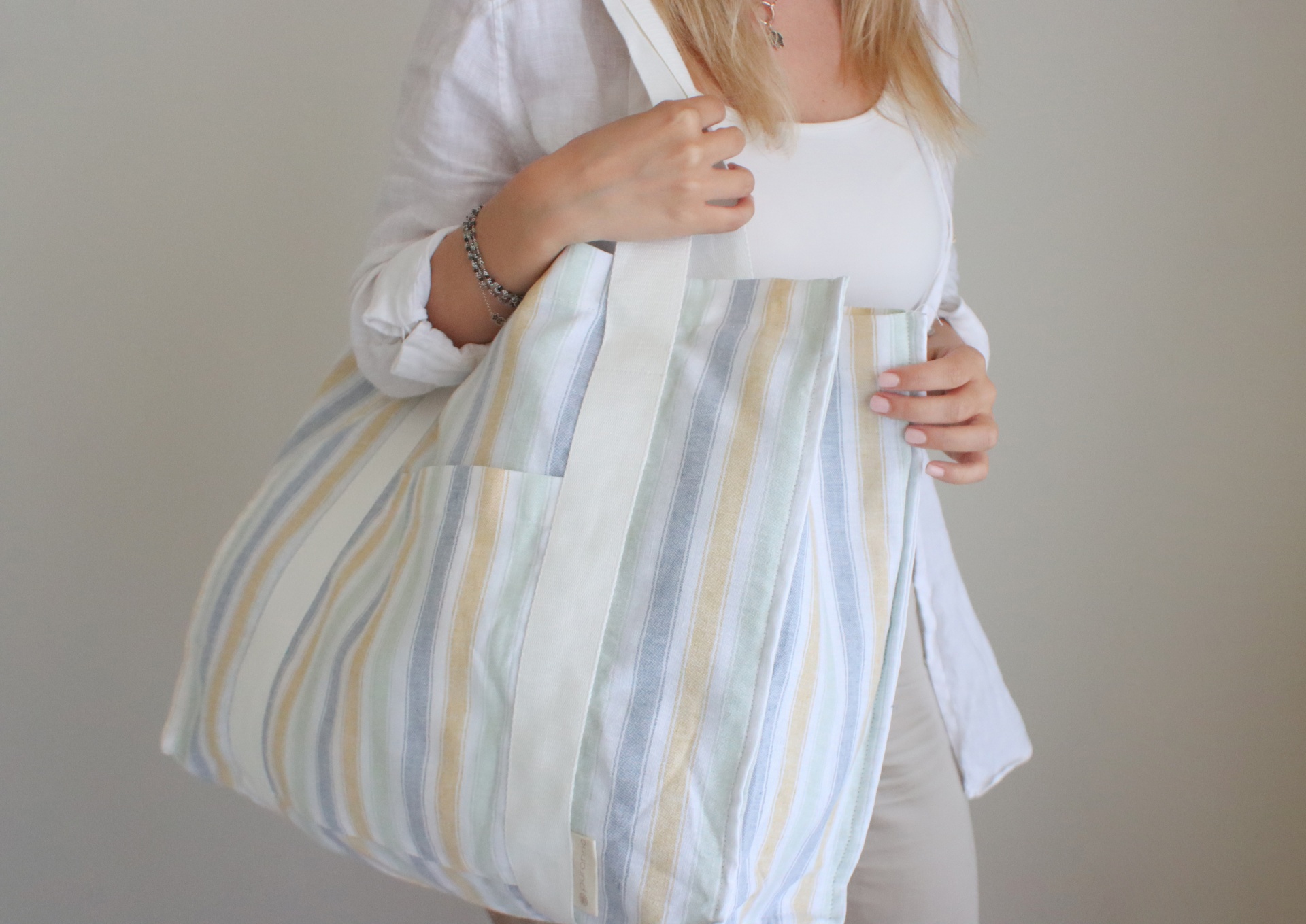 Saco de tecido listrado em tons claros com alças brancas.