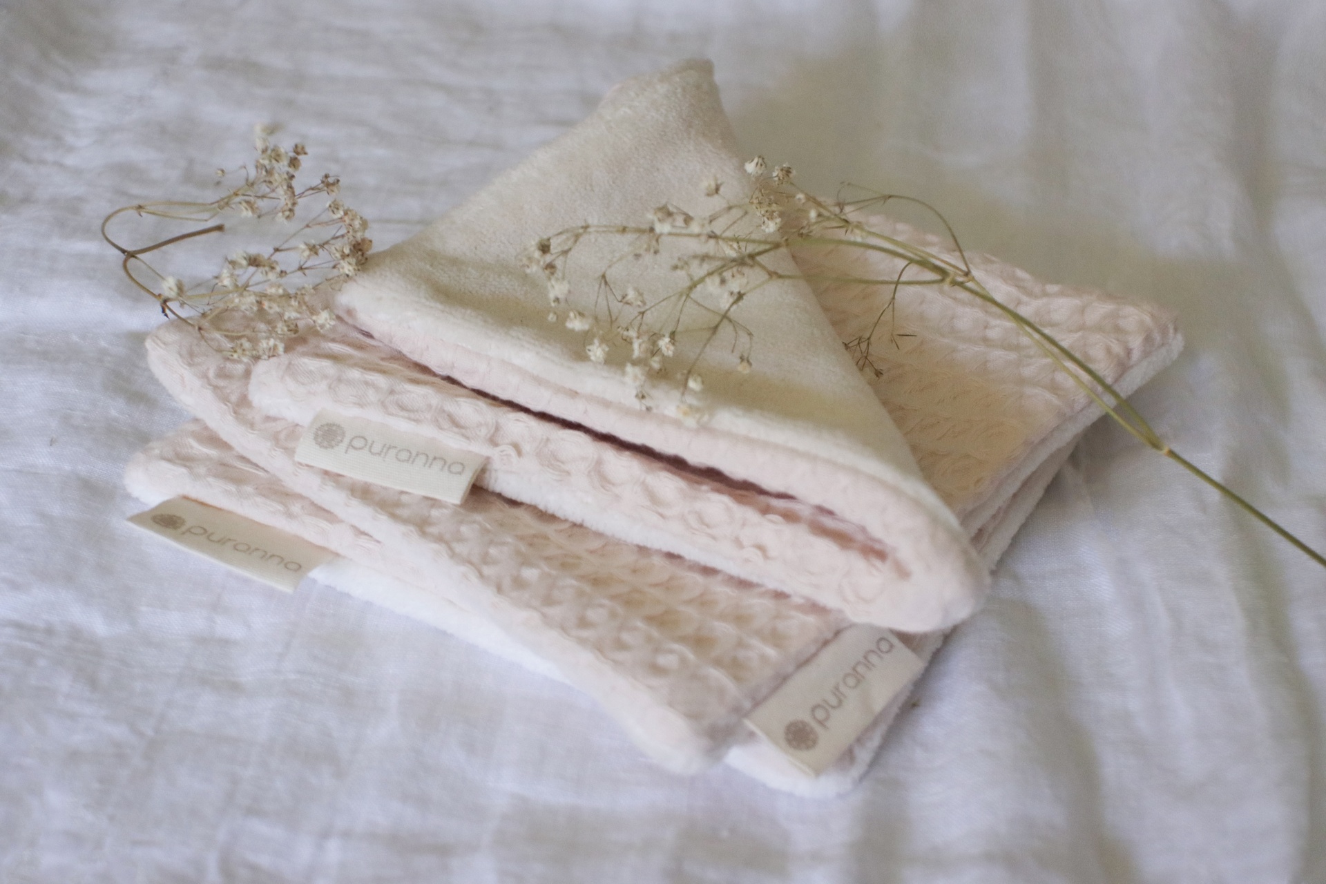 Toalhas cor de rosa claro com etiqueta Puranos e flores secas sobre tecido branco