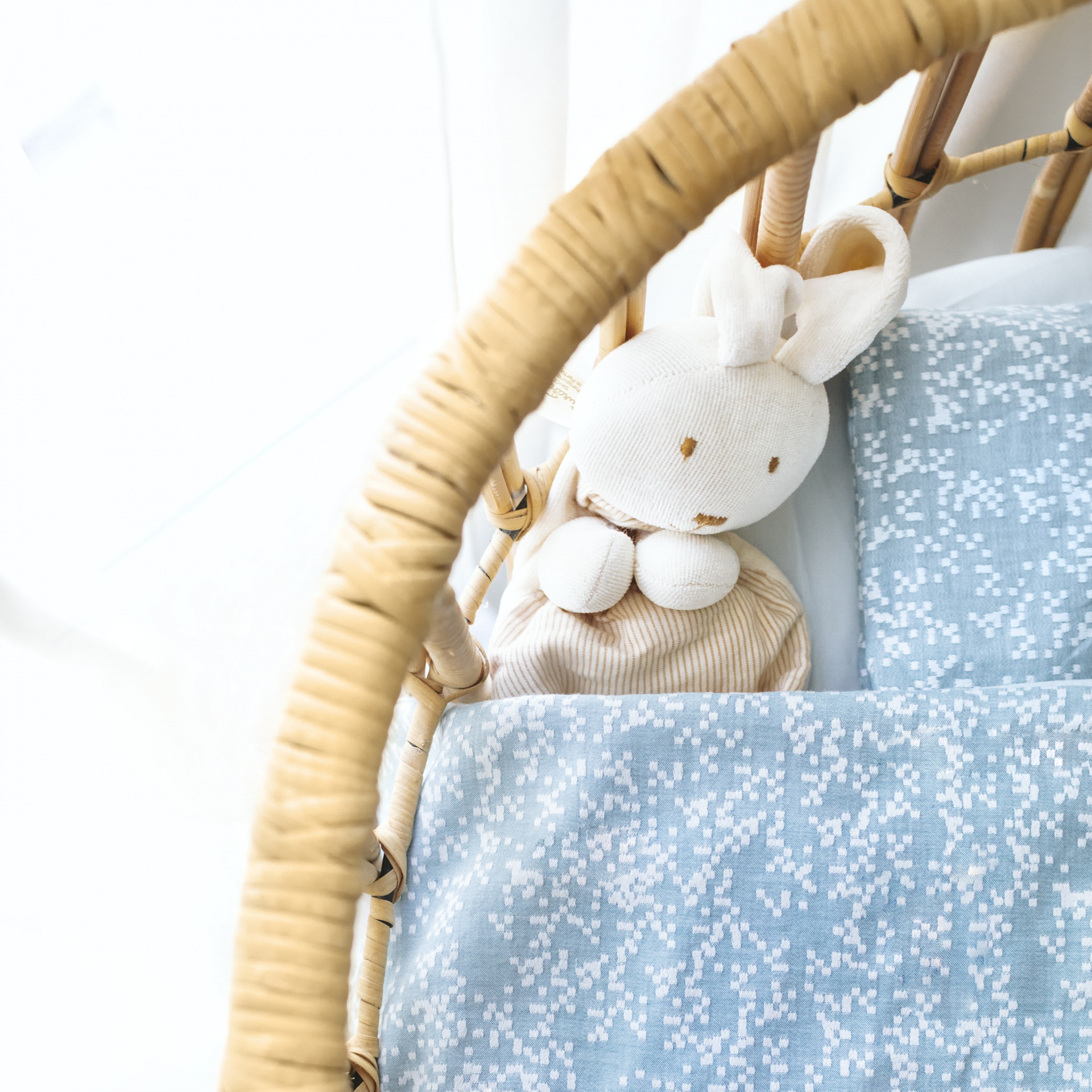 Boneco de peluche coelho numa cama com lençóis azuis e estrutura de bambu