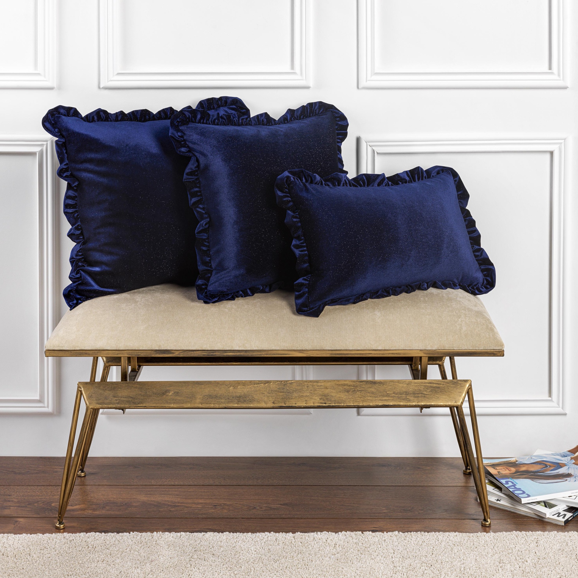 Almofadas de veludo azul escuro com bordas franzidas sobre banco estofado bege com estrutura dourada