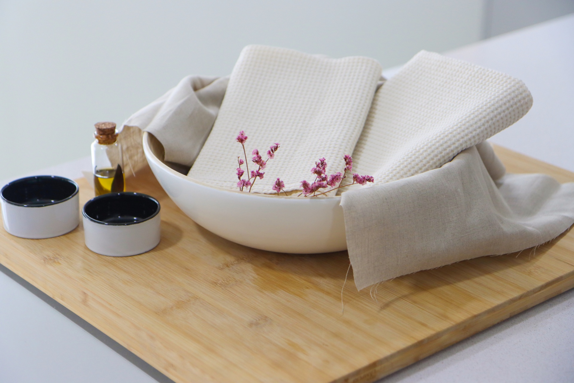 Tabuleiro de madeira com tigela branca, toalhas brancas e pequenos recipientes