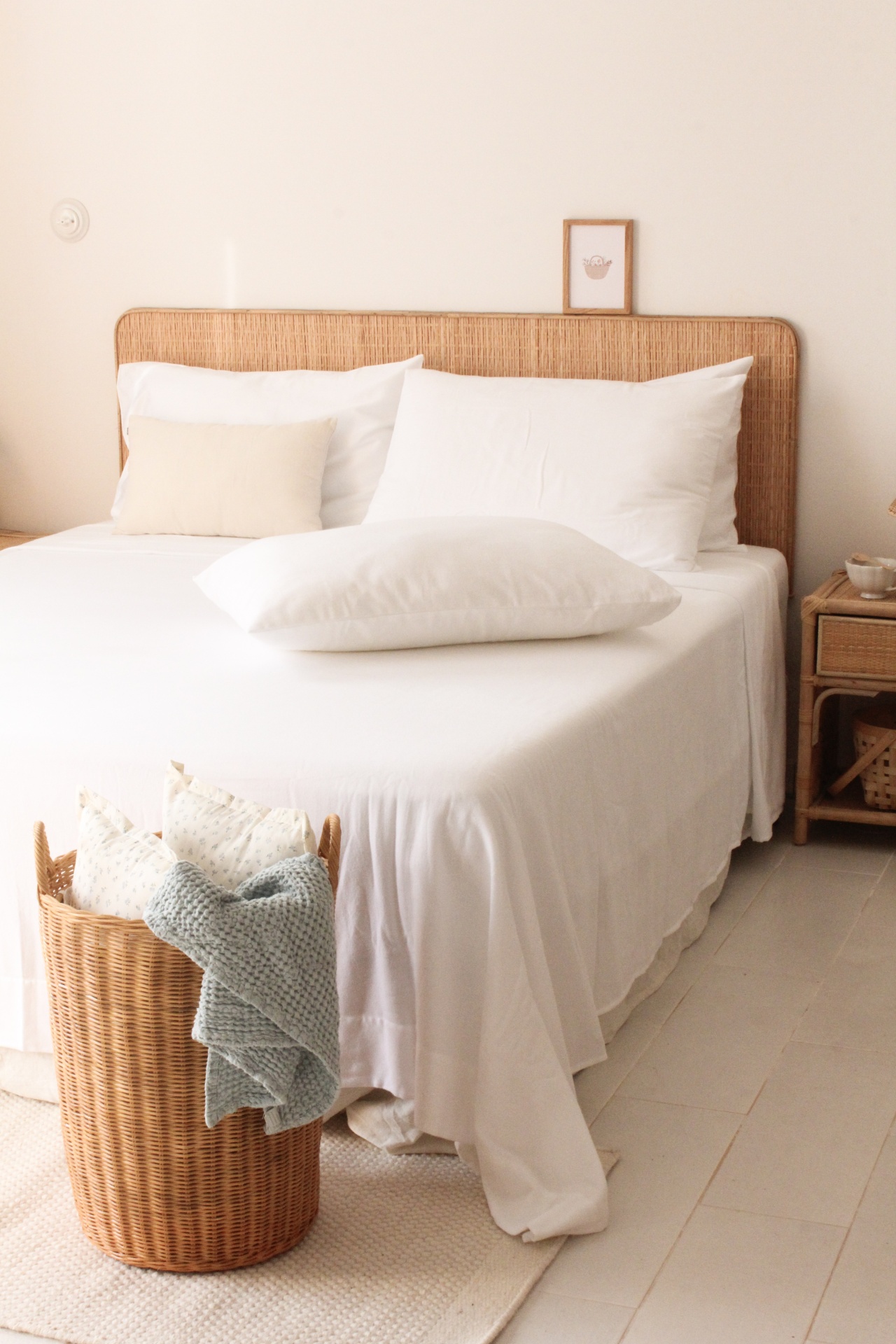 Cama com roupa de cama branca e acessórios em rattan num quarto claro