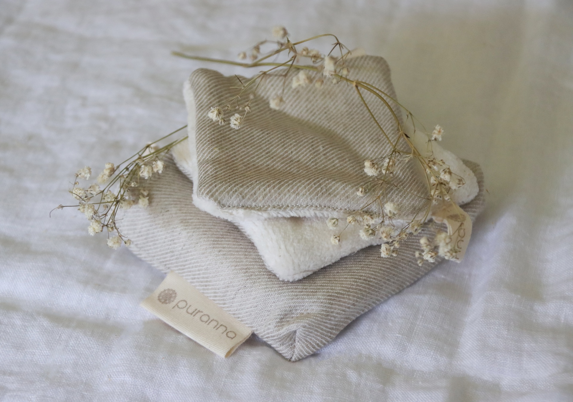 Três panos de tecido neutros com etiqueta purcotton e flores secas sobre fundo branco