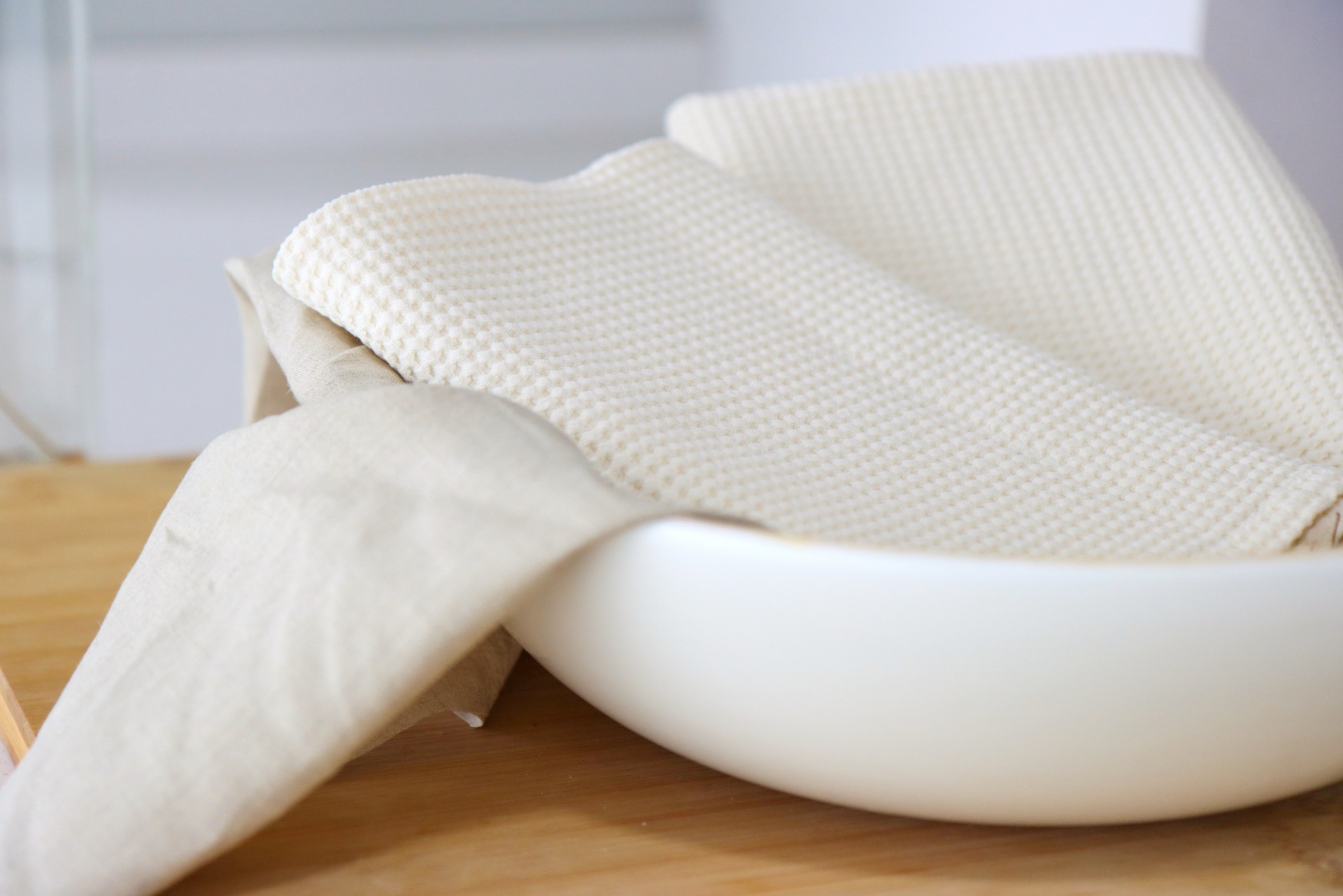 Tigela branca com tecidos beges sobre mesa de madeira clara