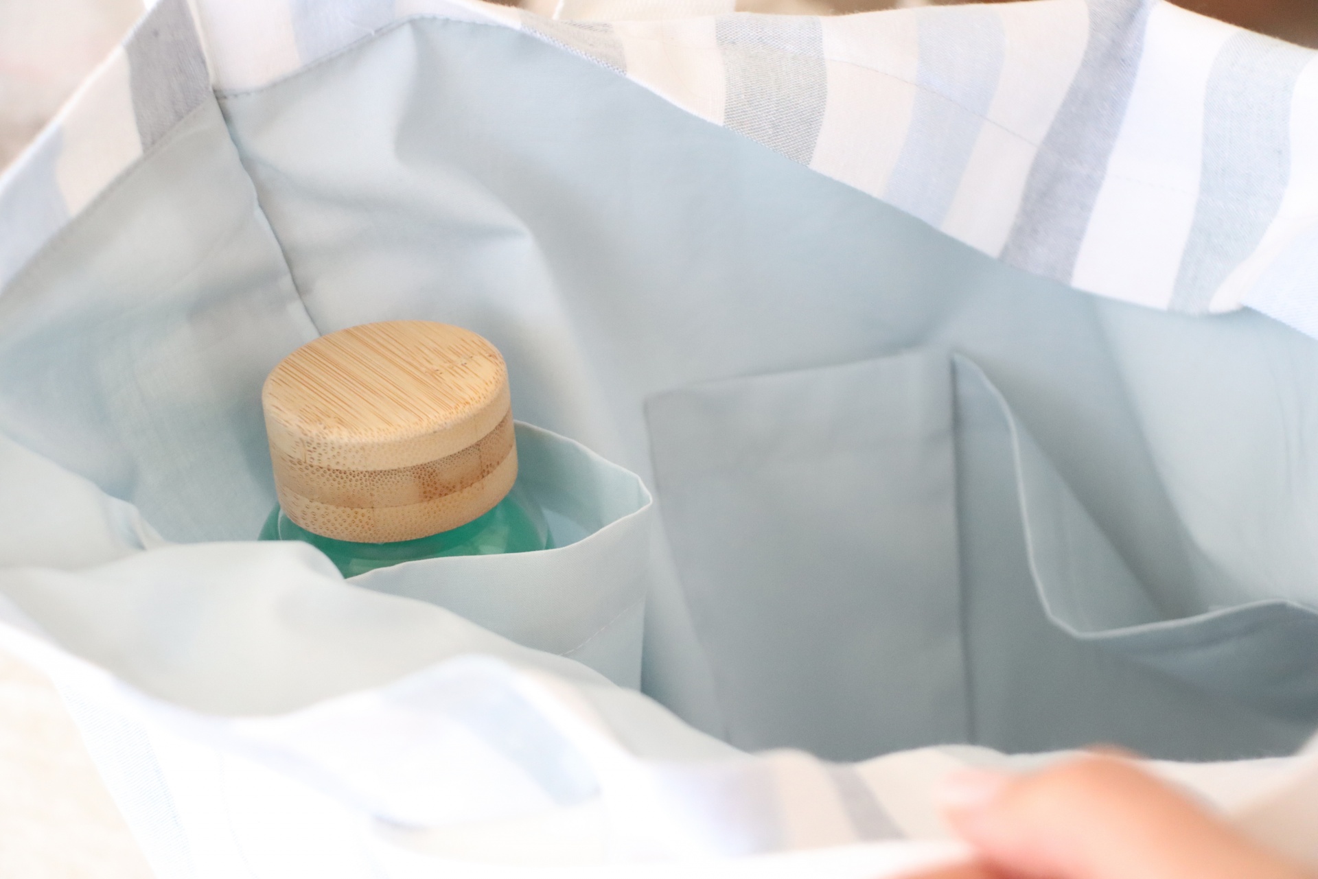 Saco de tecido às riscas azul e branco com interior cinzento e garrafa em vidro
