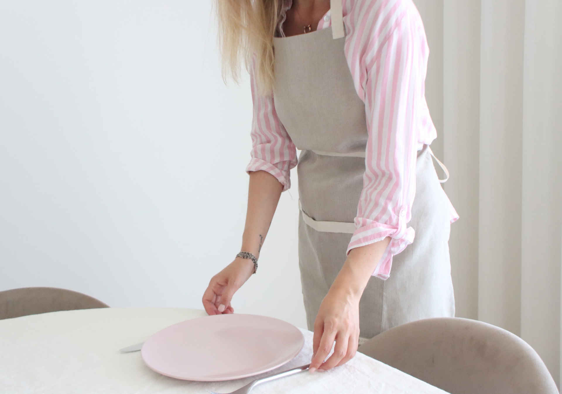 Pessoa a colocar prato rosa numa mesa com toalha branca