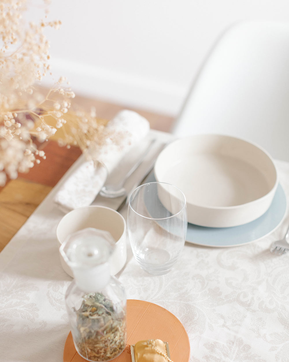 Mesa posta com prato, copos, guardanapo e jarra pequena com vegetação seca