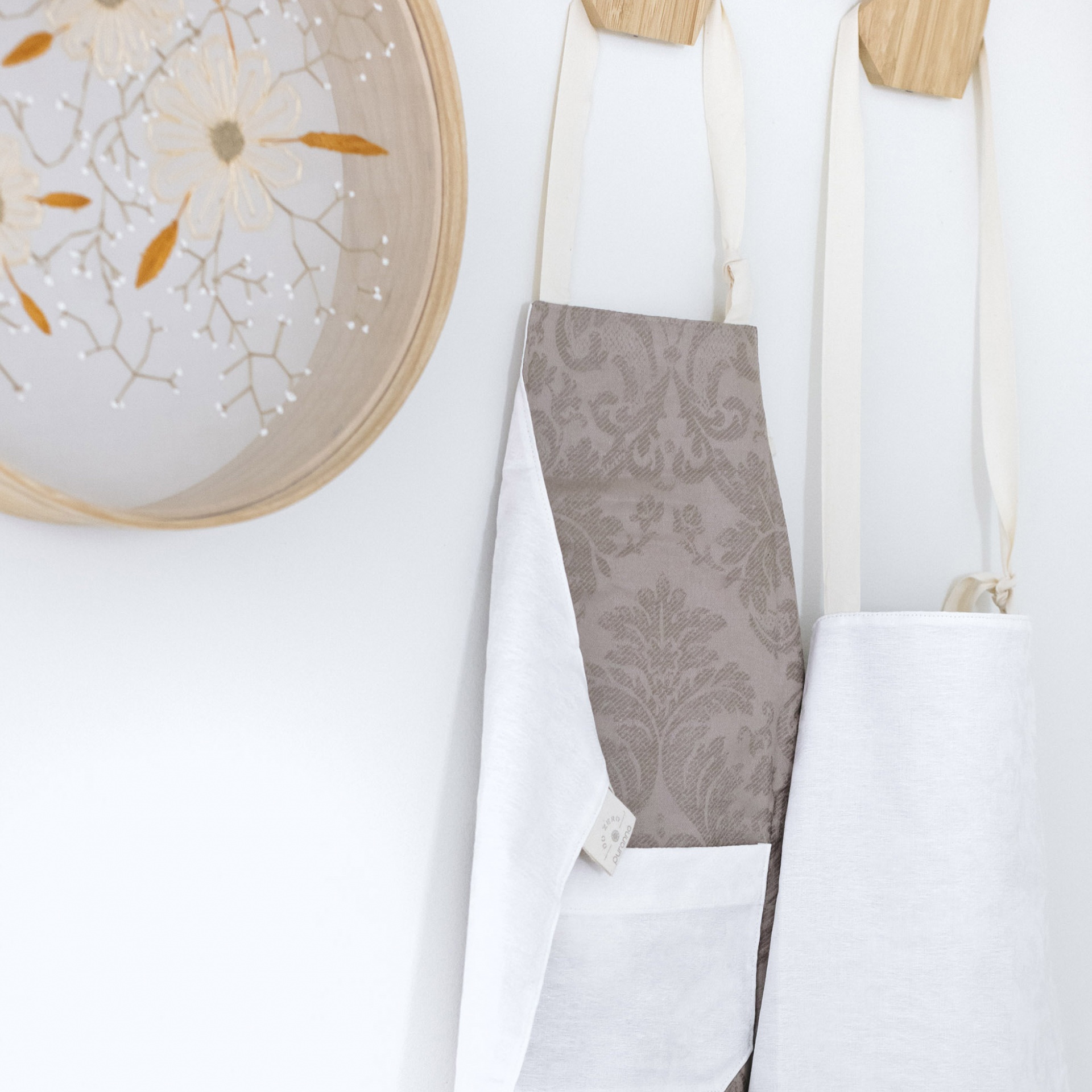 dois aventais pendurados em ganchos de madeira ao lado de uma luminária decorativa