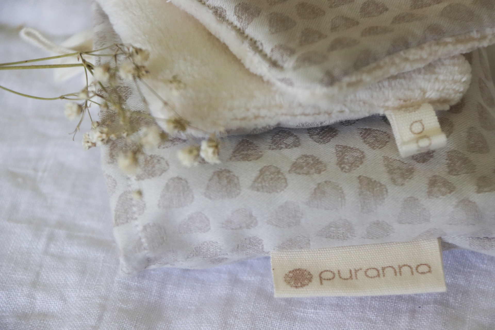 Panos de tecido creme com padrão neutro e etiquetas em cima, decorados com folhas secas