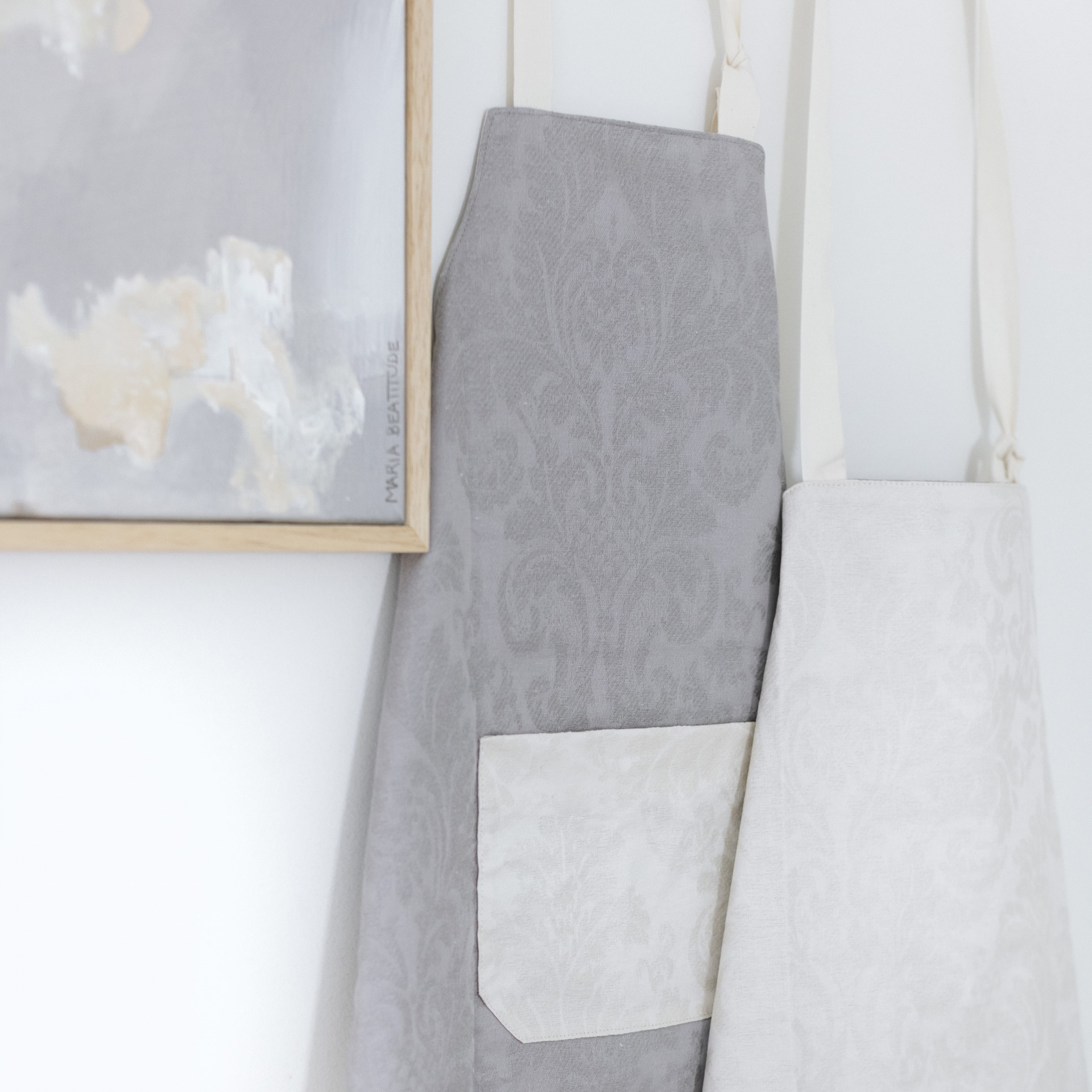 Dois aventais com padrão floral pendurados ao lado de pintura abstrata na parede.