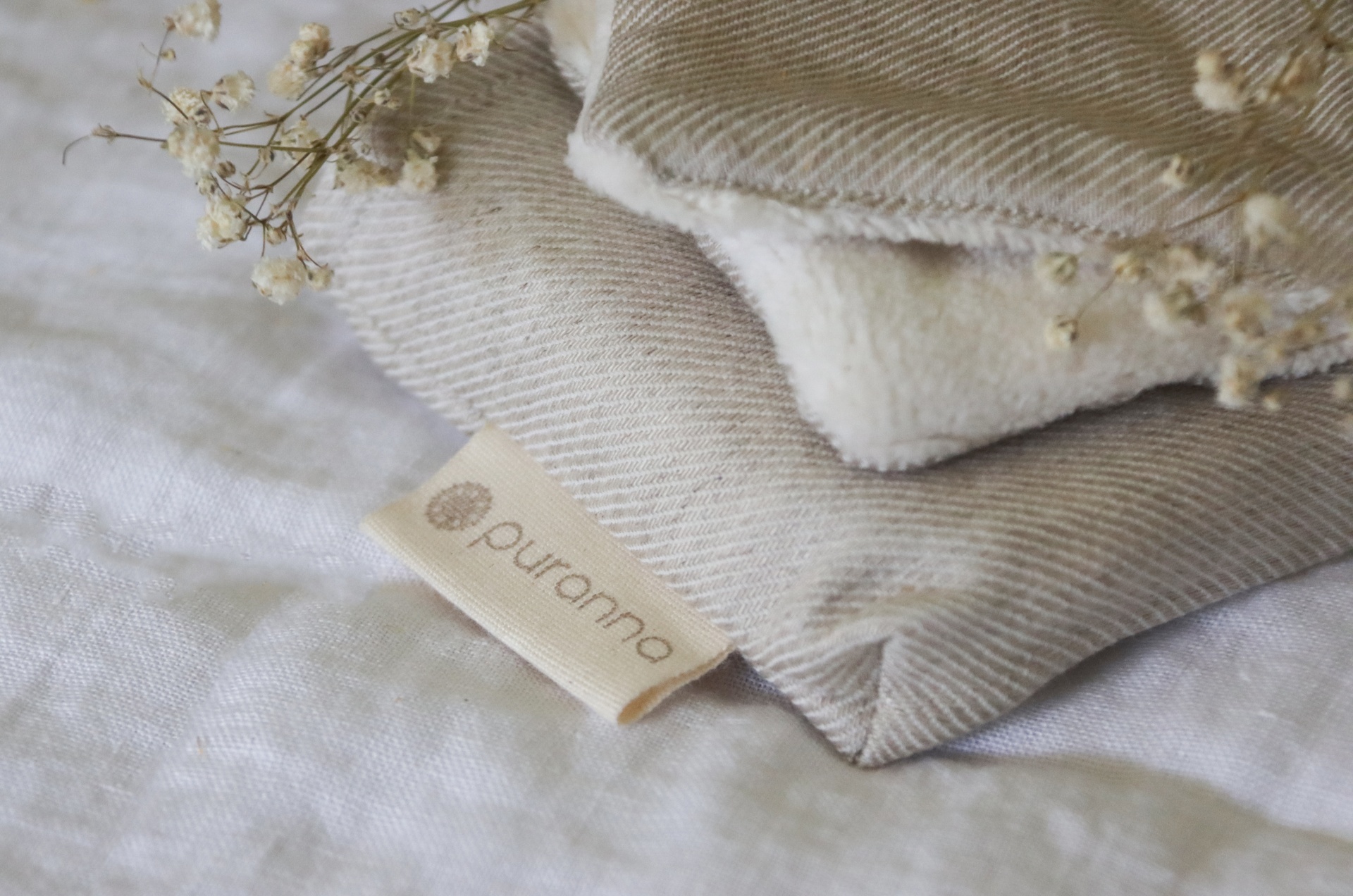 Tecidos dobrados bege e branco com etiqueta 'puranna' e ramos secos