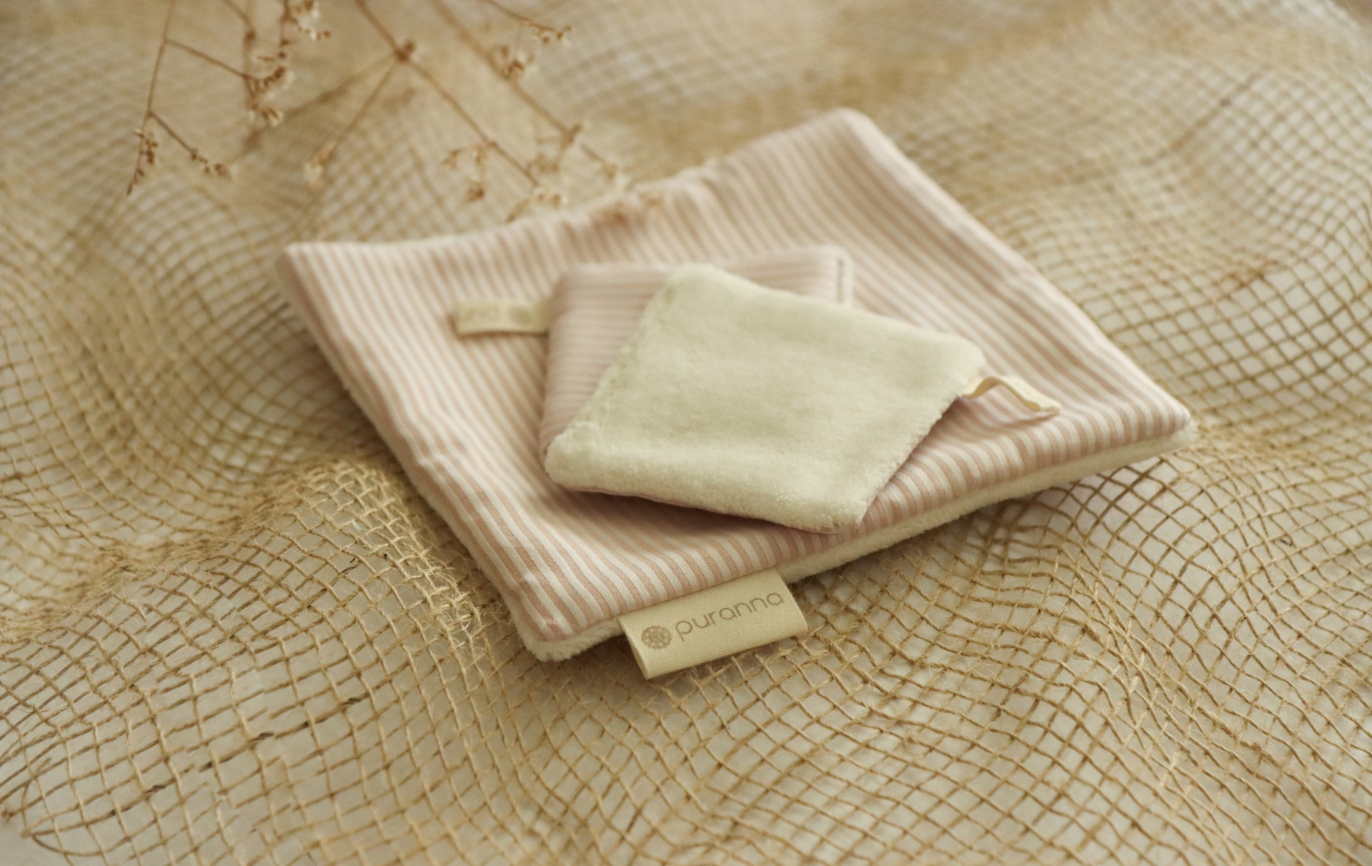 Conjunto de três toalhas pequenas creme e branco com etiqueta sobre tecido bege com padrão de rede