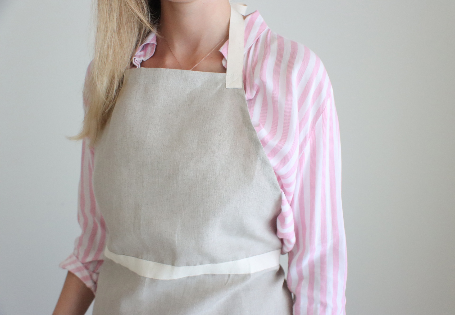 Pessoa com avental cinza claro sobre camisa riscada rosa e branca