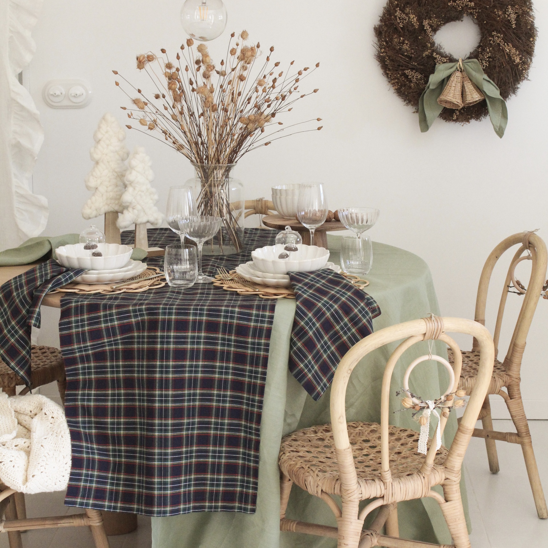 Mesa de jantar decorada com toalha verde, caminho de mesa xadrez e arranjos secos, cadeiras de vime e porcelana branca