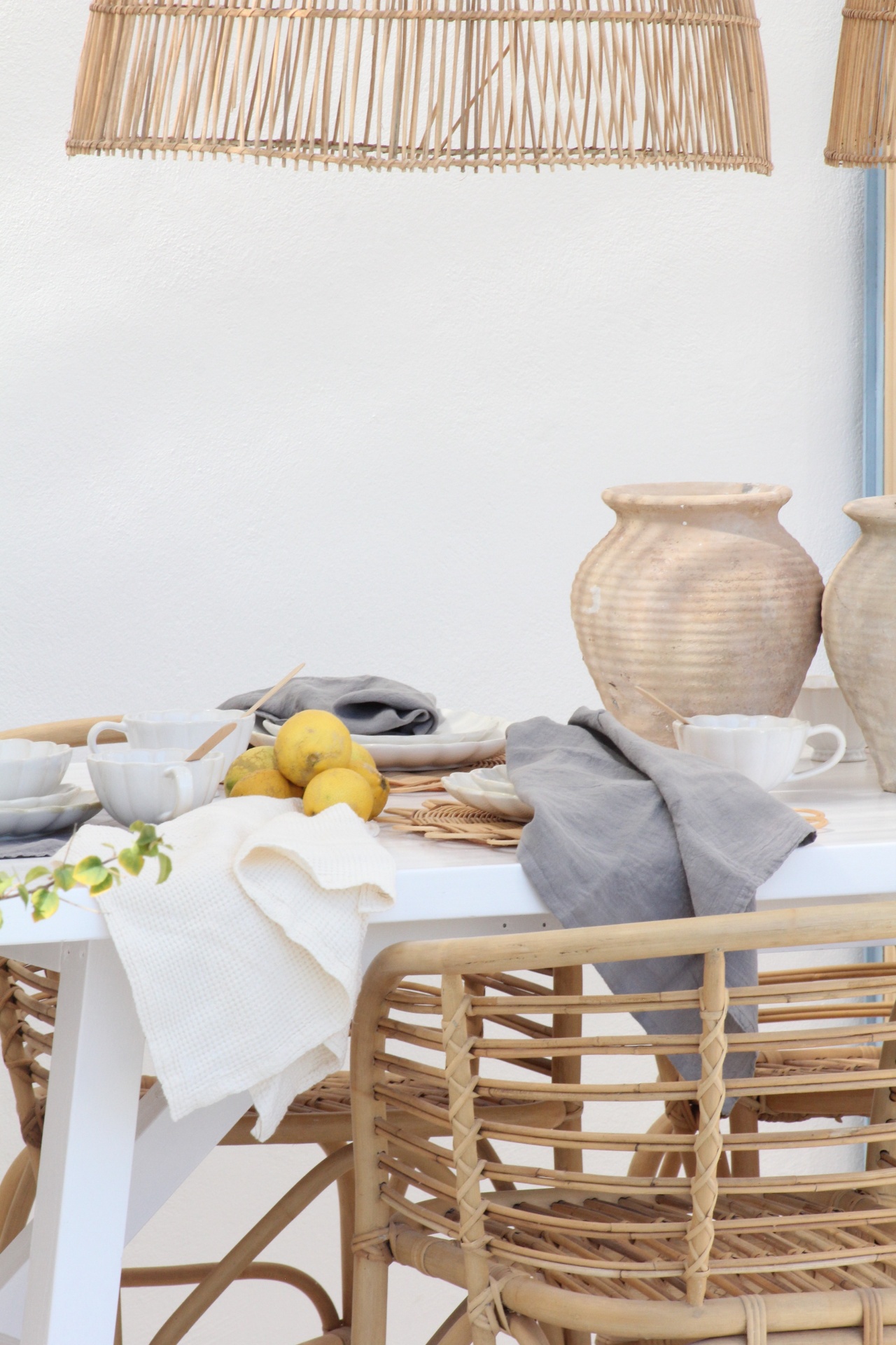 Mesa de jantar branca com jarras de cerâmica e cadeiras de verga
