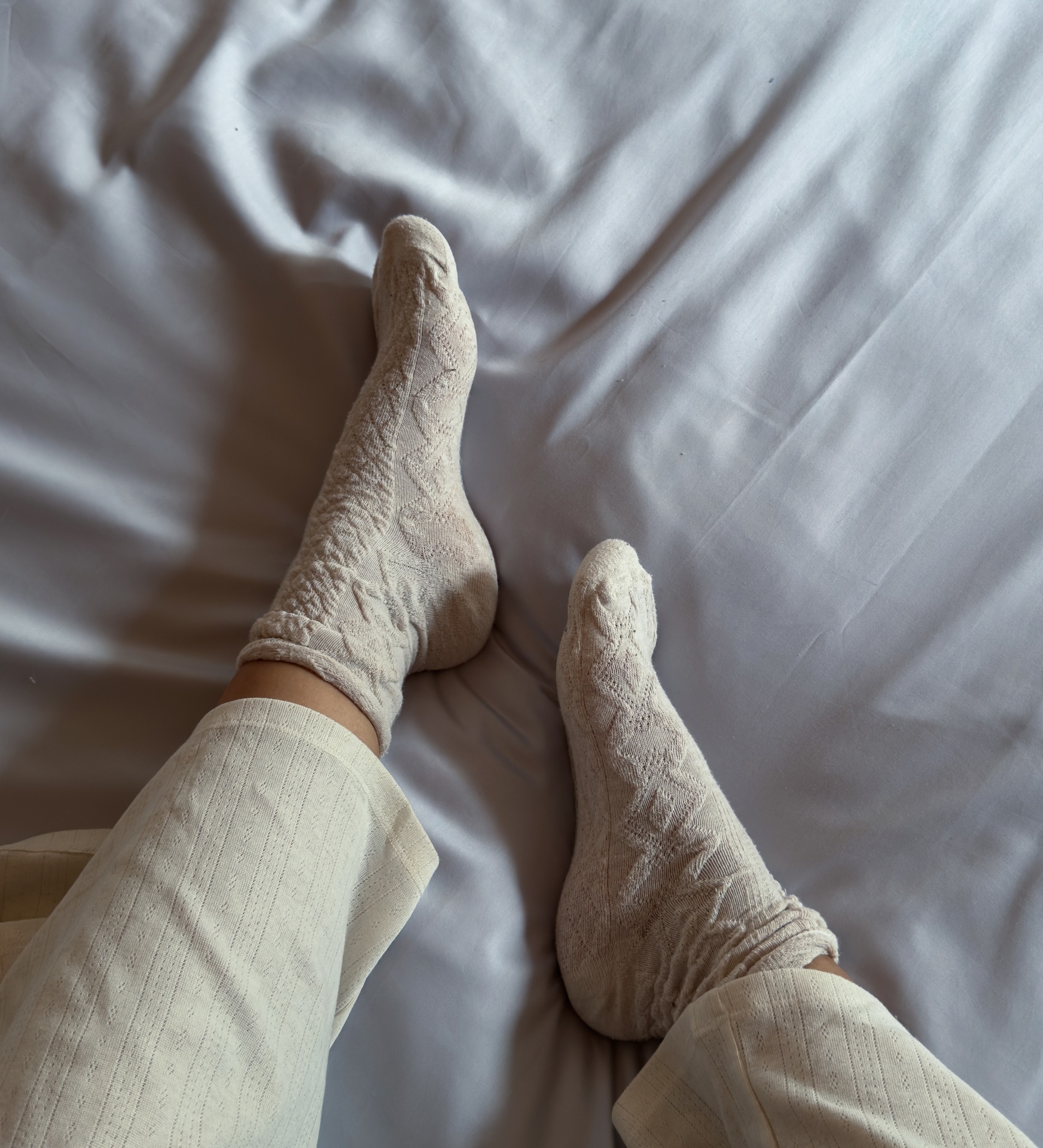 Meias bege com padrão de malha usadas num ambiente interior com lençol branco.