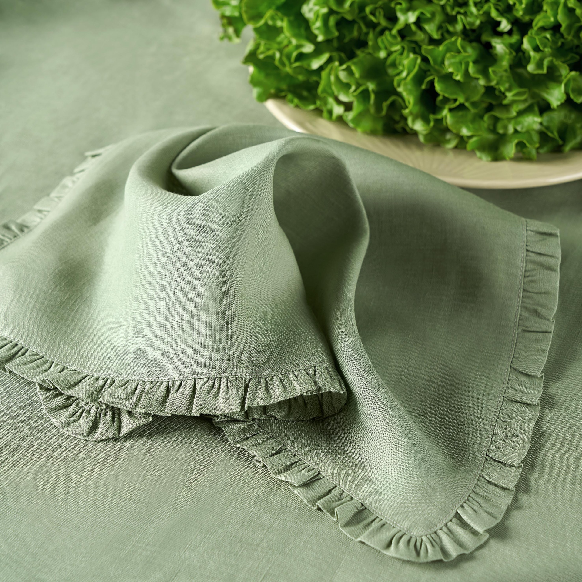 Guardanapo verde claro com bainha frisada ao lado de uma tigela com alface