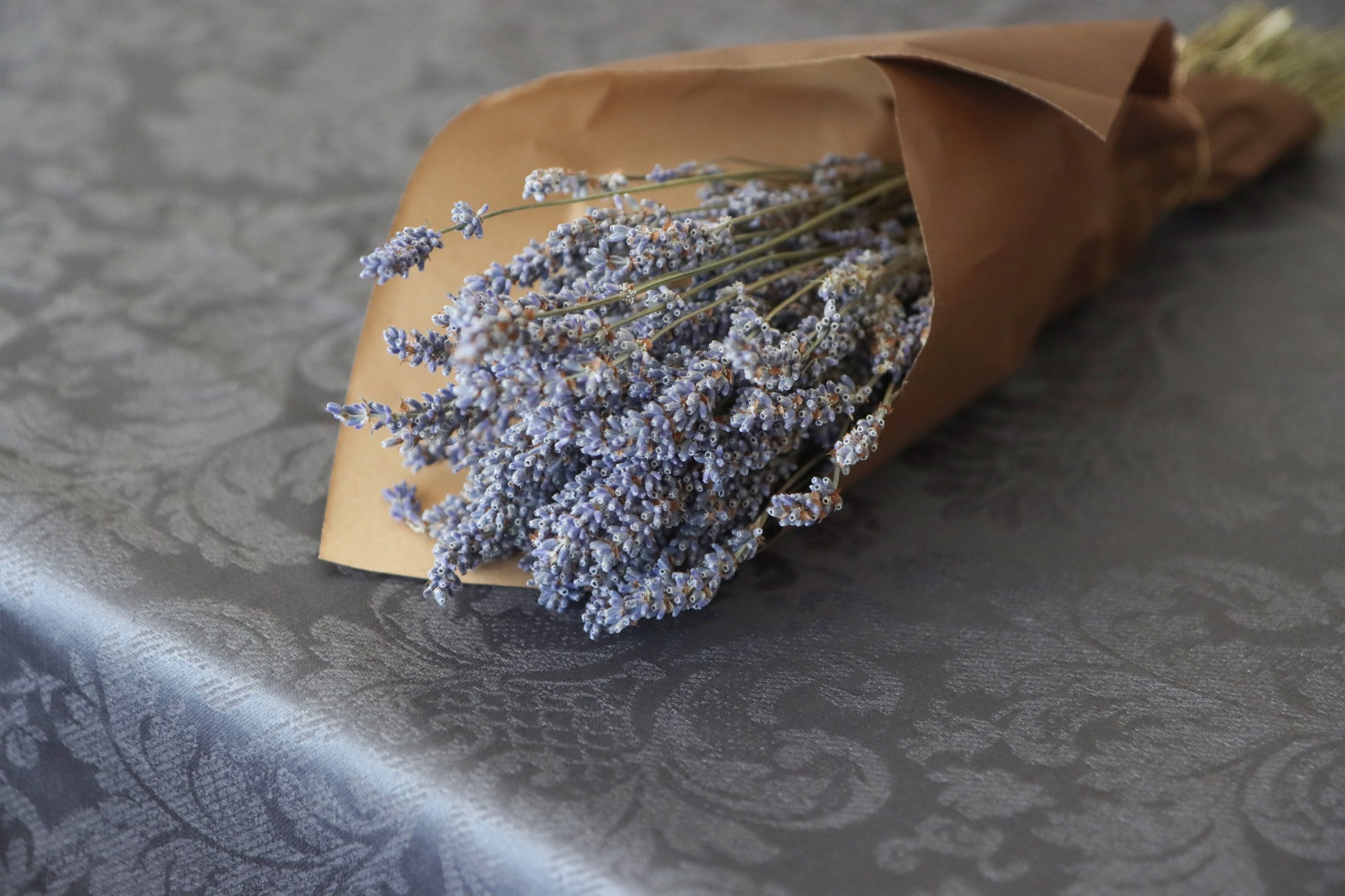 Ramo de flores secas envolto em papel castanho sobre toalha cinza com padrão