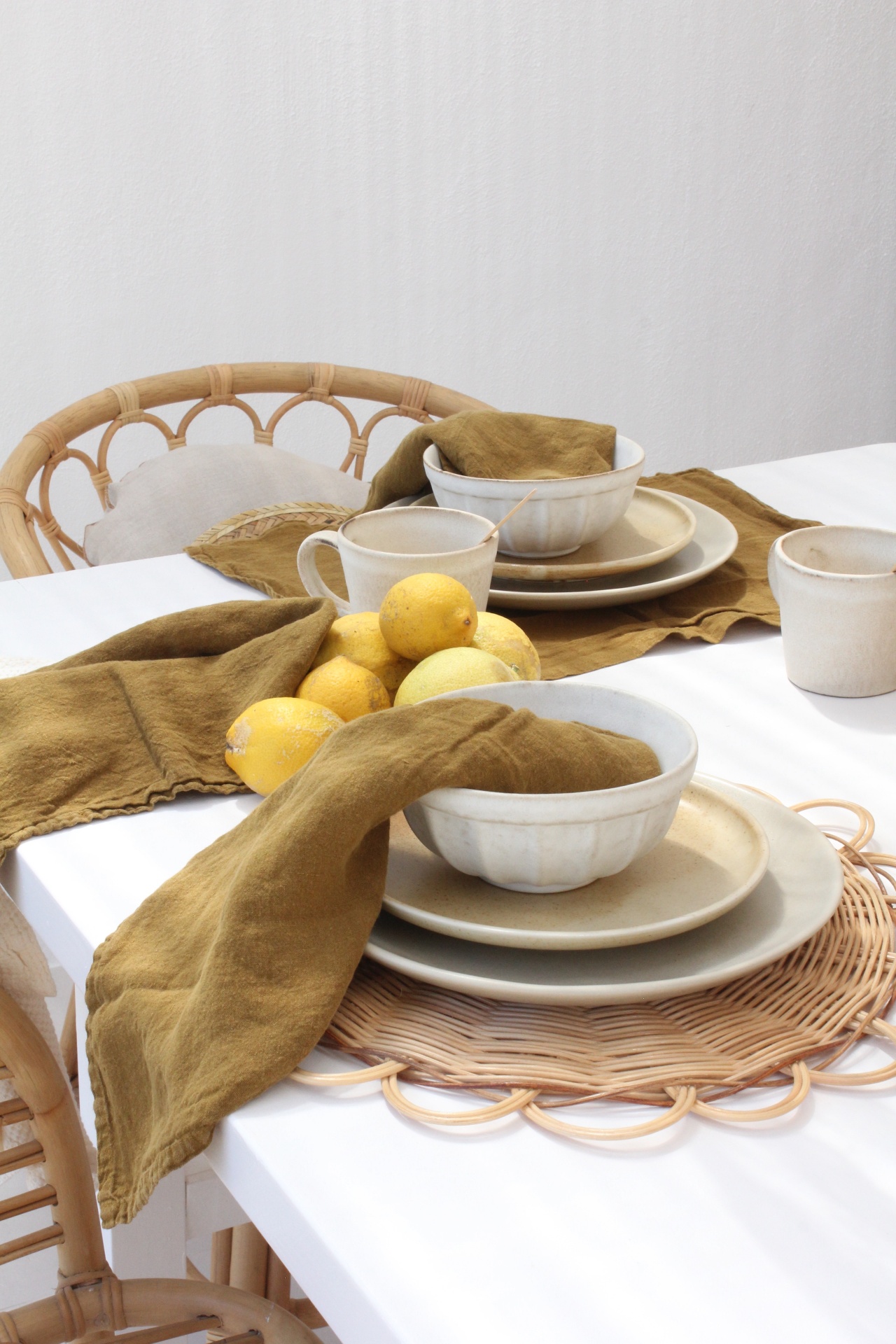 Mesa posta com louça bege, guardanapos verdes e limões sobre mesa branca