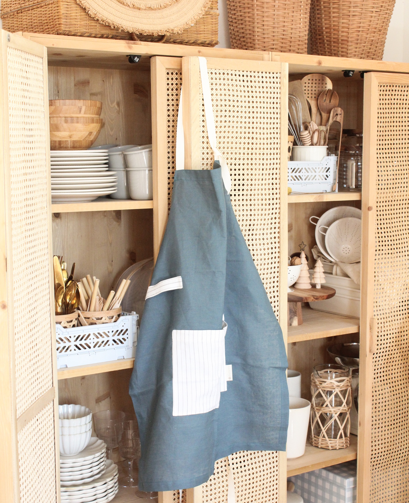 Armário de madeira com avental azul pendurado e utensílios de cozinha organizados
