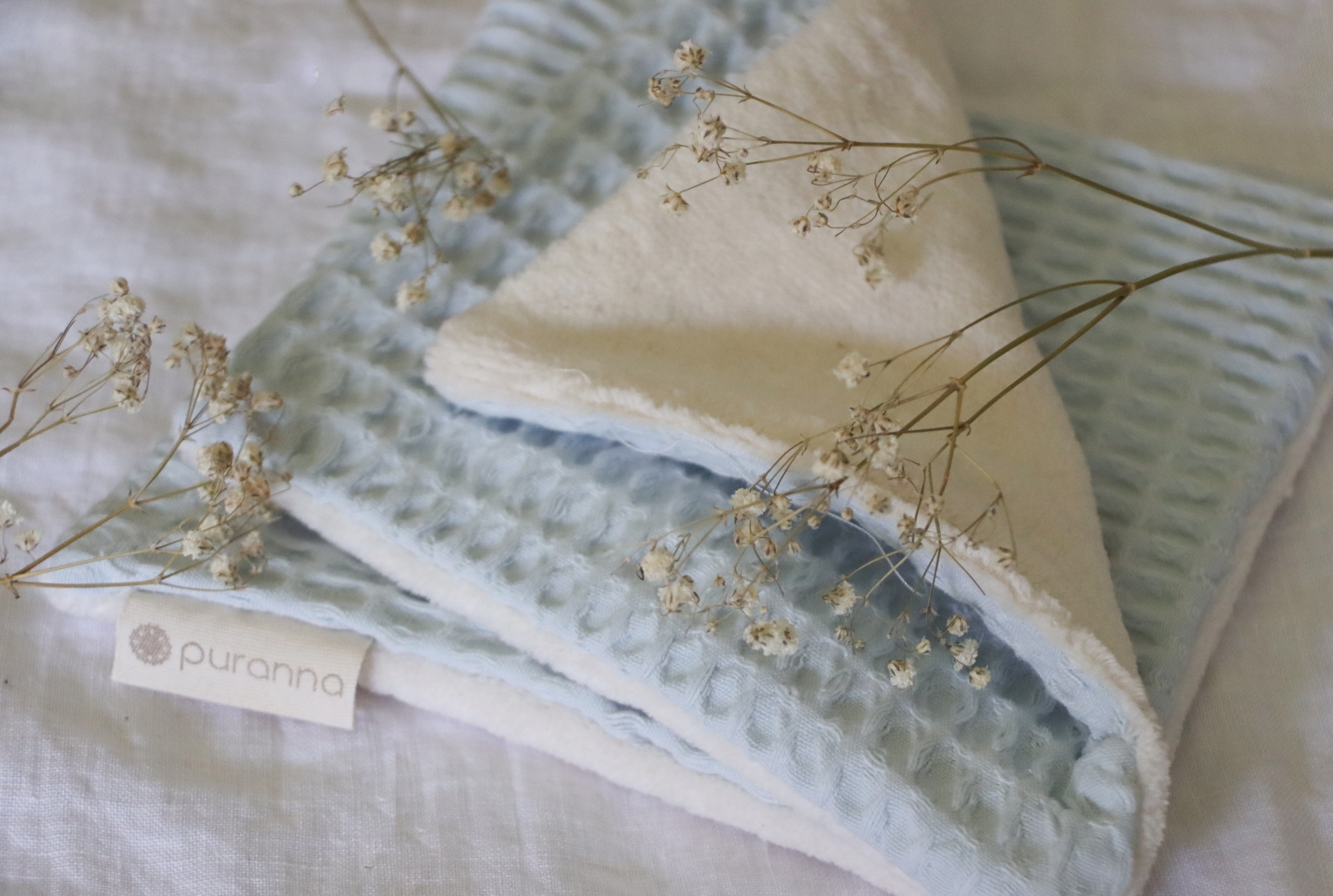 Toalha ou manta azul claro com padrão de favo e interior branco sobre tecido branco