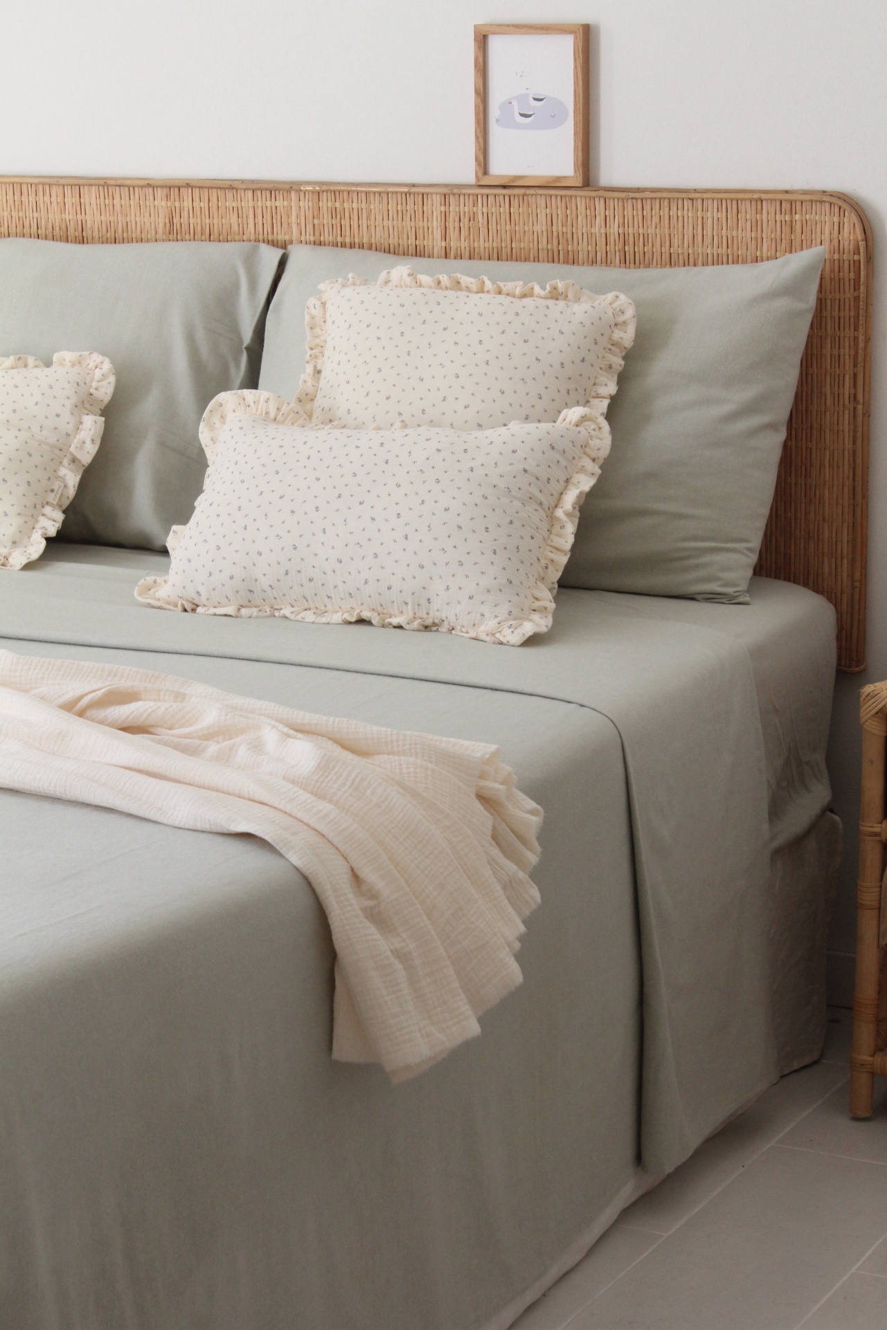 Cama com lençóis cinza claro, almofadas decorativas creme, cabeceira de vime clara e manta creme