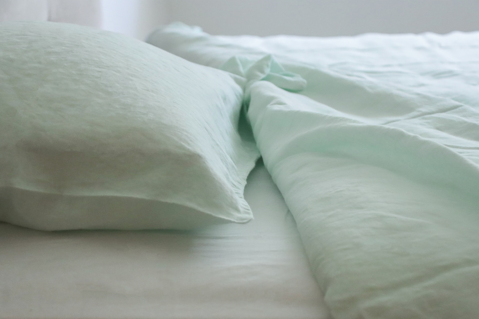 Almofada e lençol verde claro em cama, colchão branco