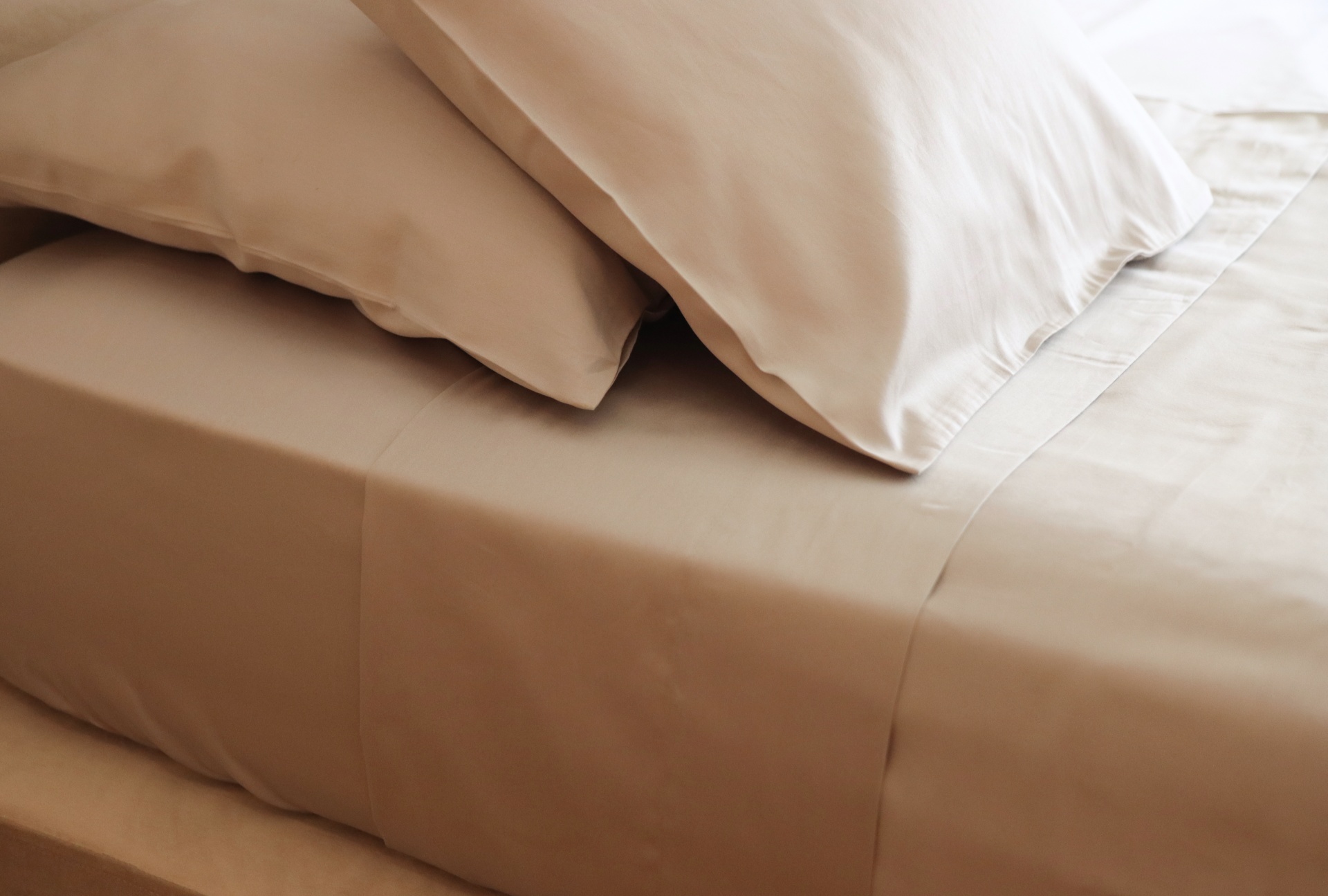 Conjunto de cama bege com lençol e fronhas em tecido liso