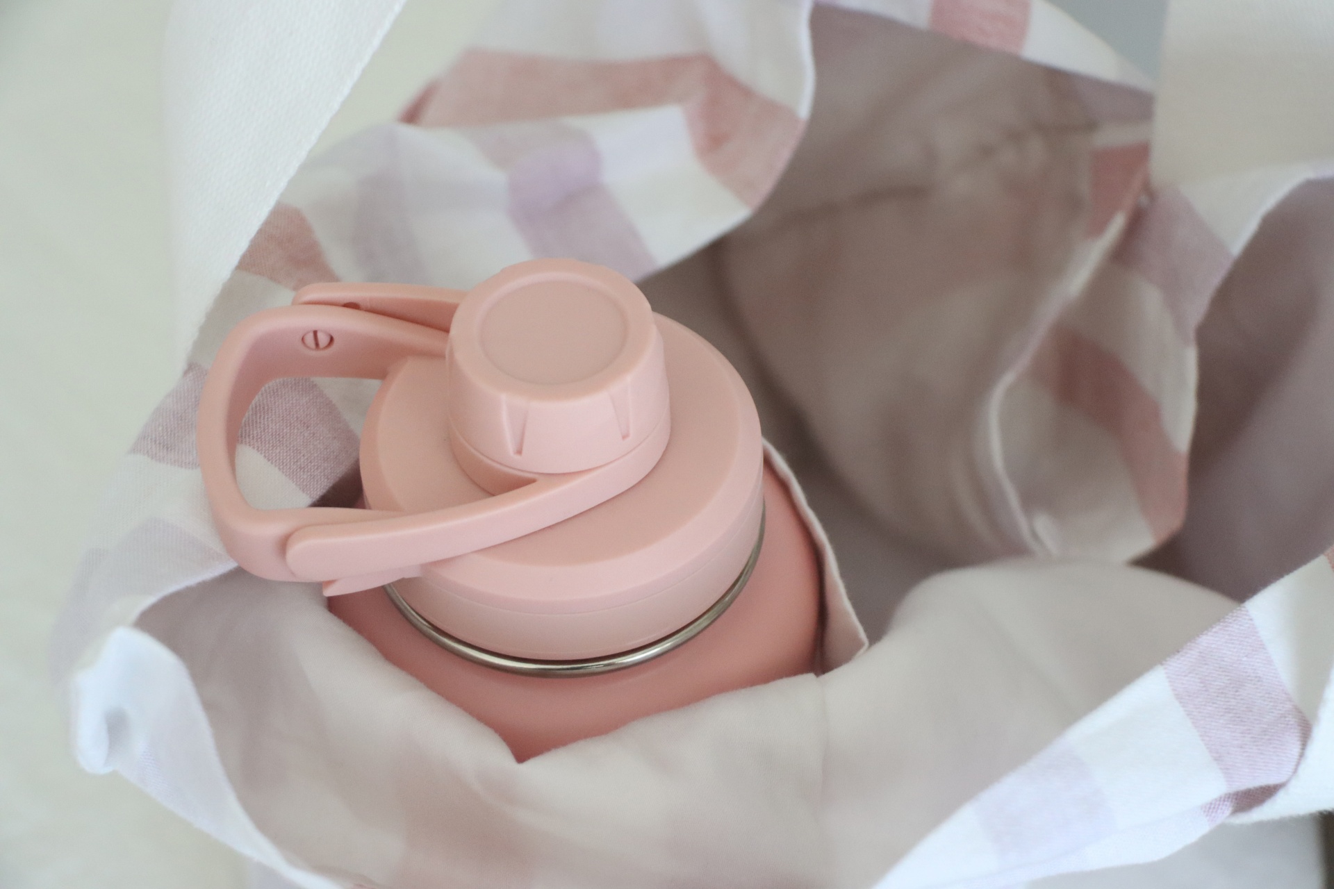 Garrafa térmica cor-de-rosa com tampa e alça, sobre tecido branco com riscas cor-de-rosa
