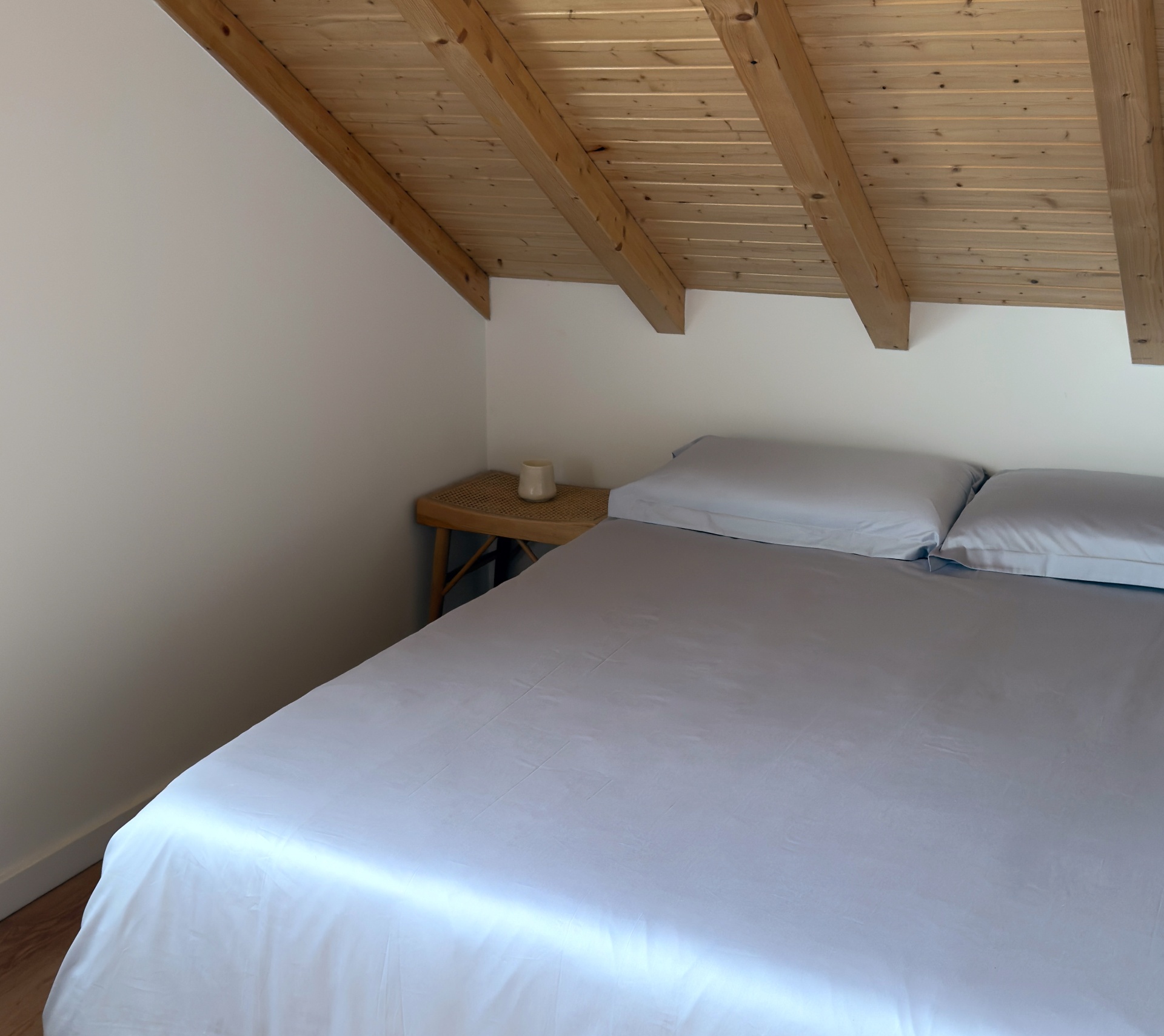 quarto com cama de casal branca e teto de madeira inclinado