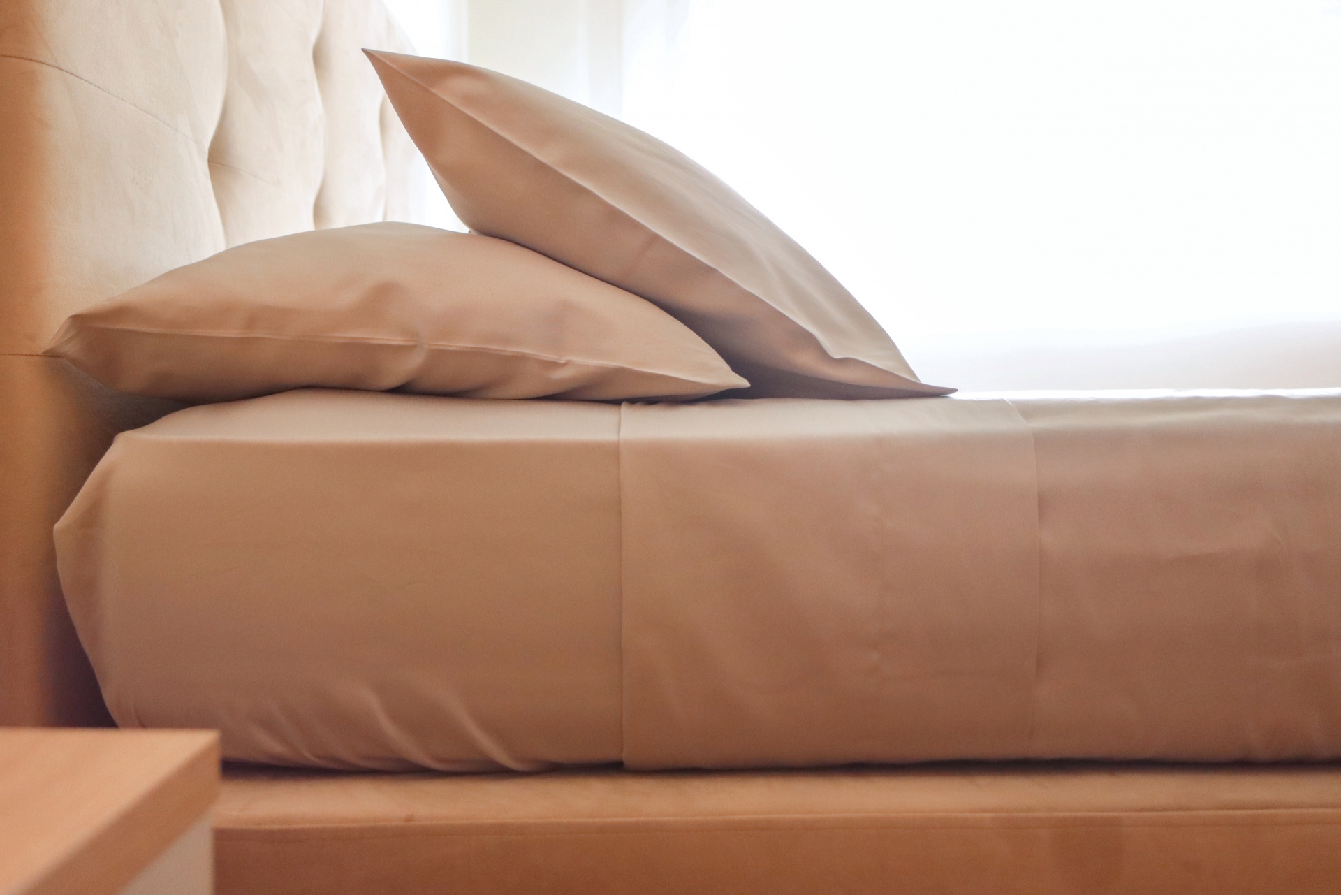 Conjunto de cama bege com almofadas e lençol lisos num quarto claro