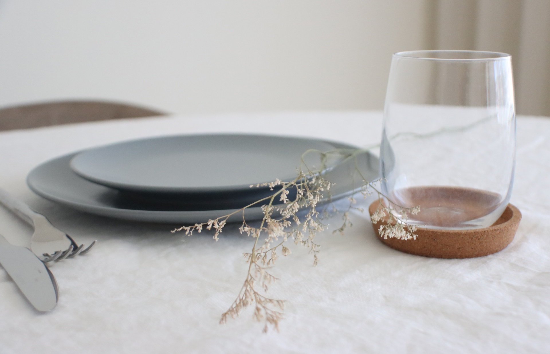 Conjunto de pratos, copo de vidro, suporte castanho e talheres sobre mesa com toalha branca