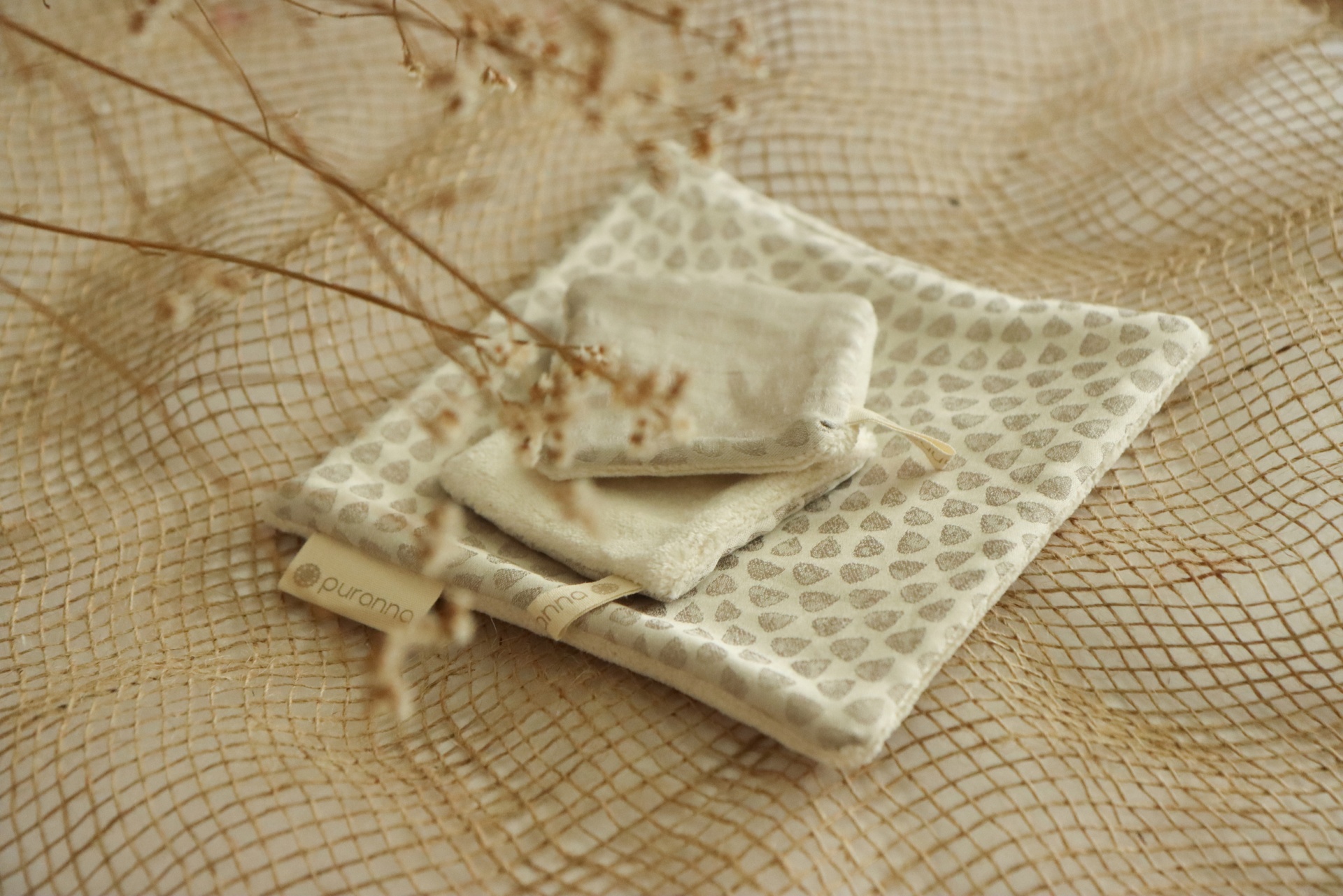 Três saquinhos de tecido bege com padrão de folhas sobre rede dourada