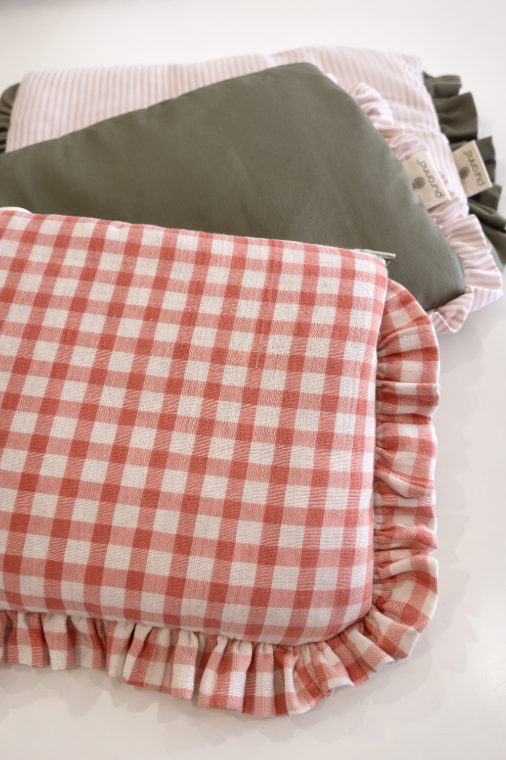 Quatro almofadas decorativas de algodão, duas às riscas rosa e branco com folhos, duas verdes lisas com etiquetas puramon.