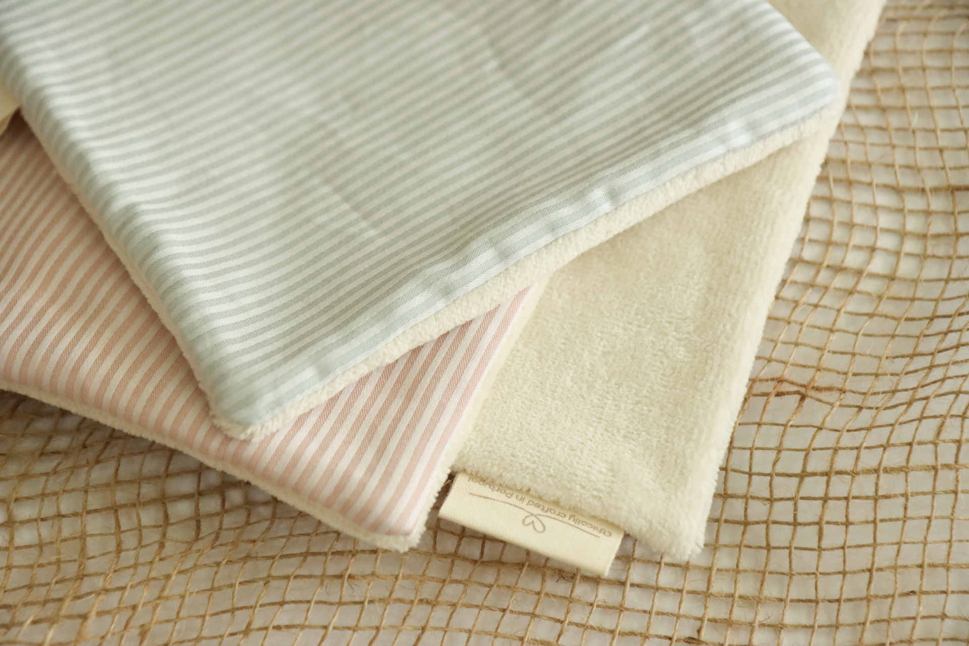 Tecidos de bebé em tons neutros dobrados sobre superfície com padrão de rede