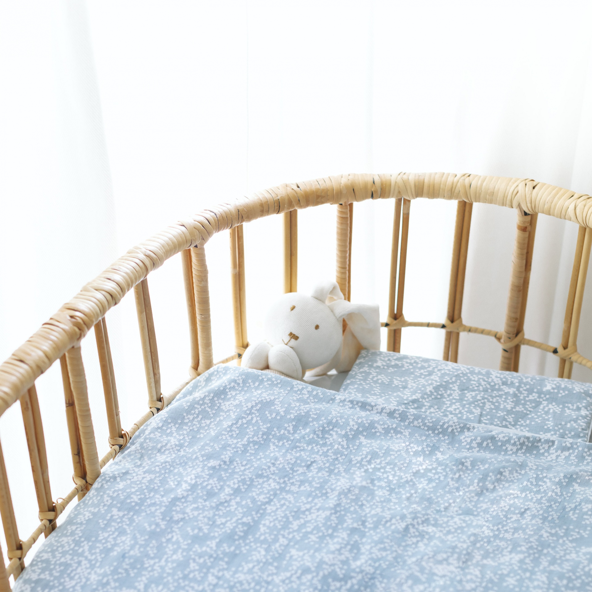 Berço de bebé em vime com tecido azul claro estampado e peluche coelho branco