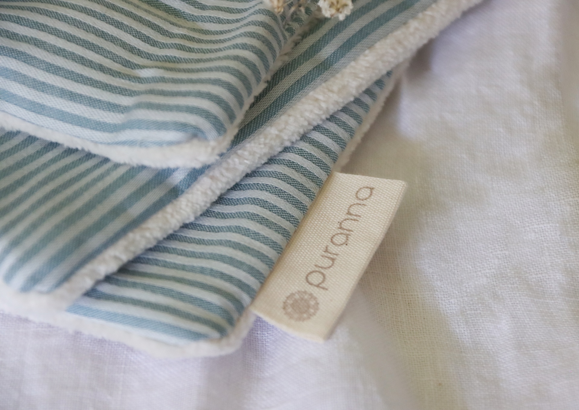 Tecido riscado azul e branco com etiqueta 'purama' sobre tecido branco.