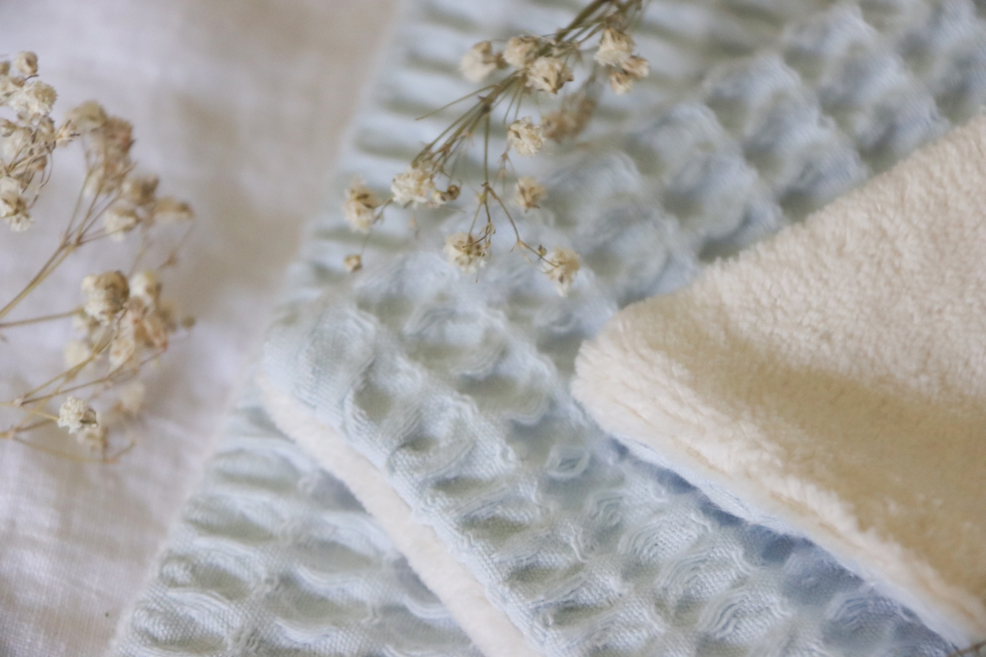 Toalhas azuis com padrão de relevo e toalha branca macia com flores secas