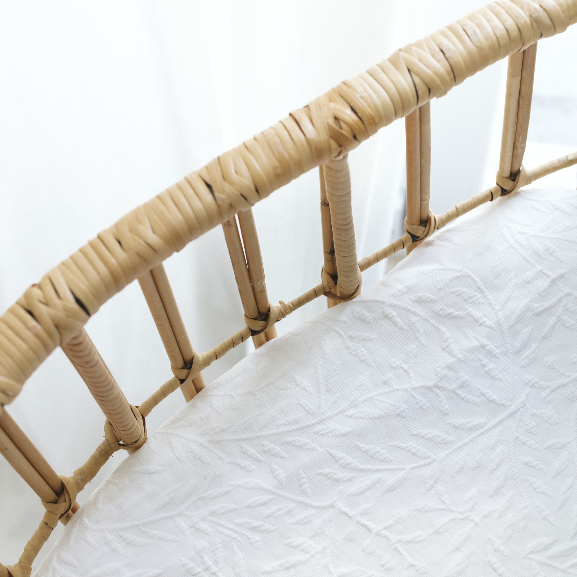 Berço ou cama de bebé com estrutura em vime e colcha branca texturizada